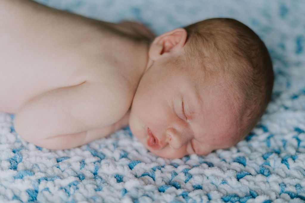 Newborn baby sleeping peacefully on blue textured blanket.