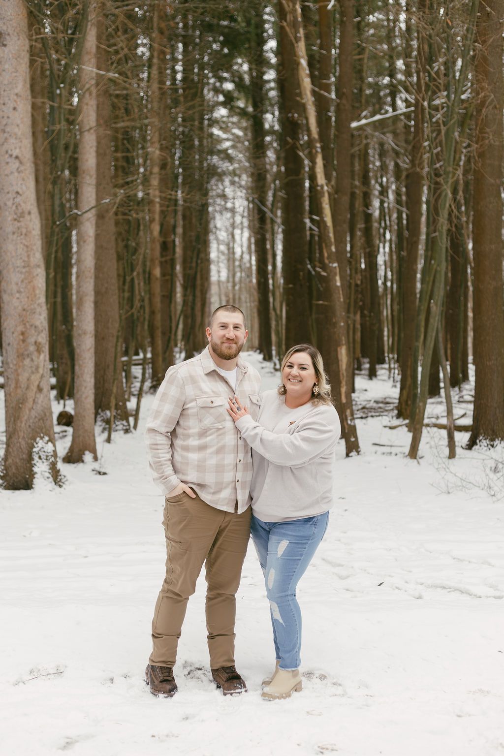 A joyful couple poses together in a snowy forest setting.