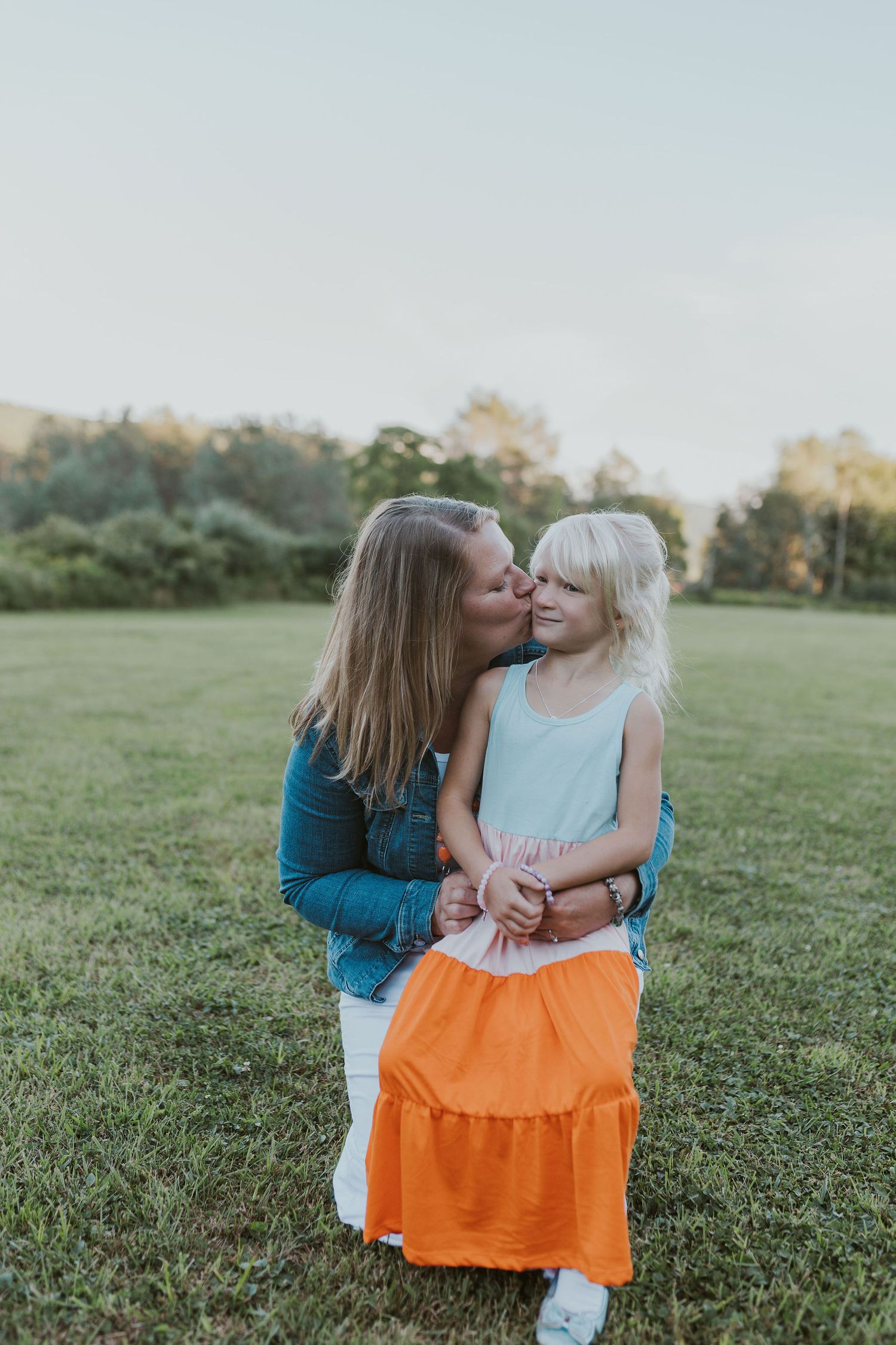 Sweet moment between parent and child in matching orange and blue outfits on grassy field.