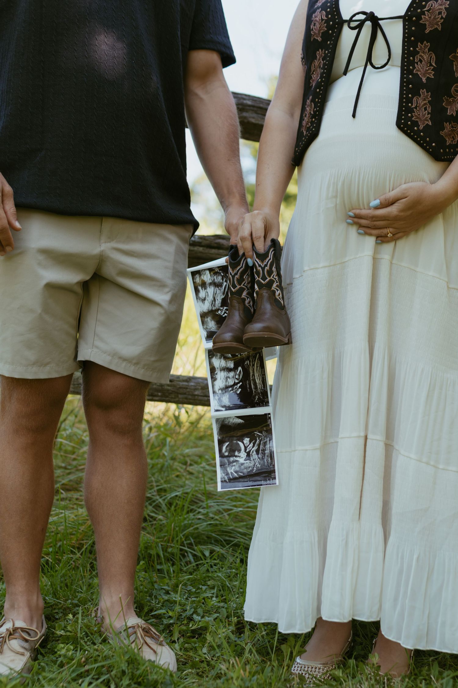 Pregnant couple holding ultrasound photos and tiny cowboy boots outdoors, maternity announcement photo session.