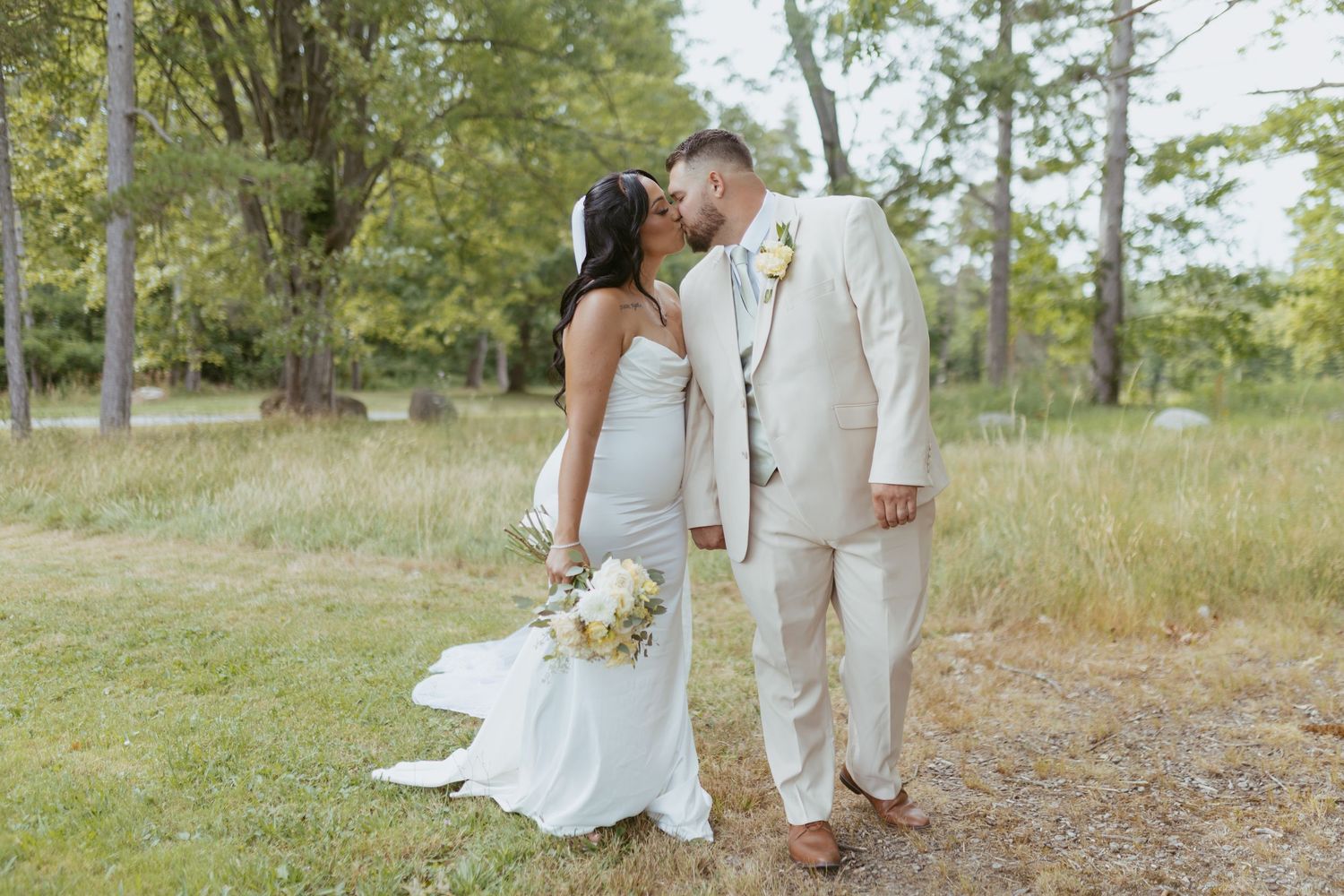 Bride and groom share a romantic kiss on a garden path surrounded by lush trees on their wedding day.