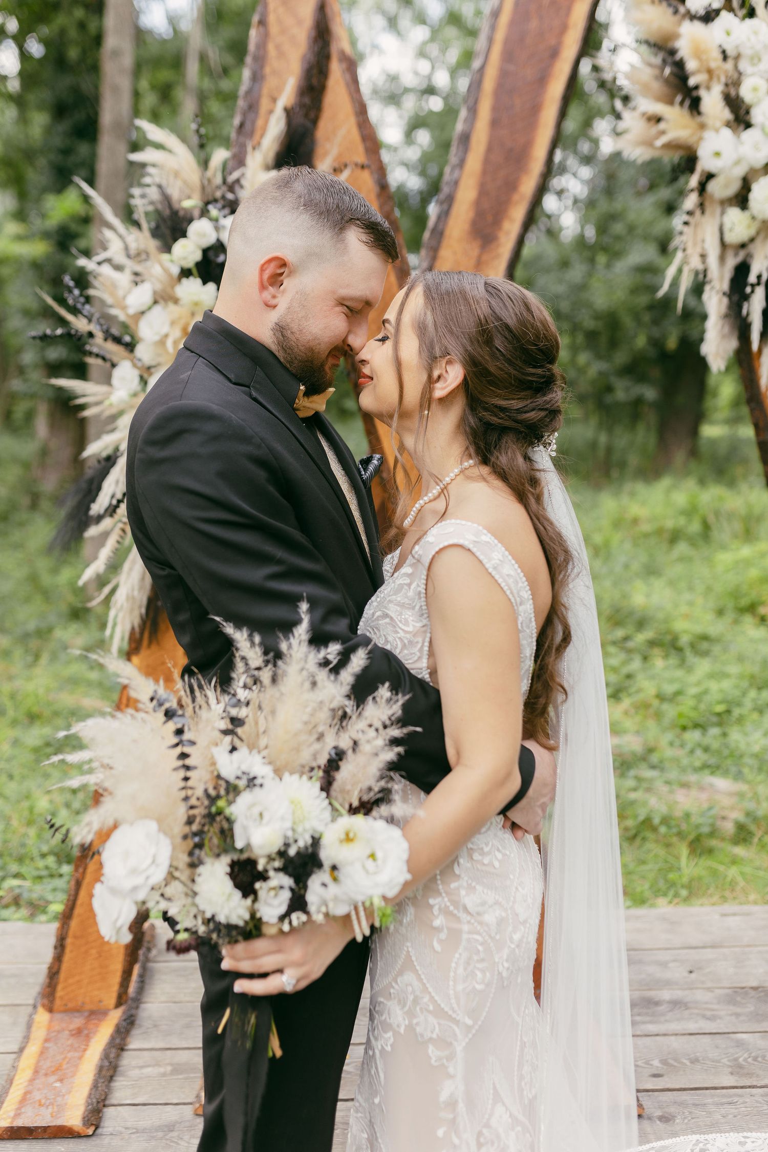 Couple sharing romantic moment under rustic wooden arch decorated with dried flowers.