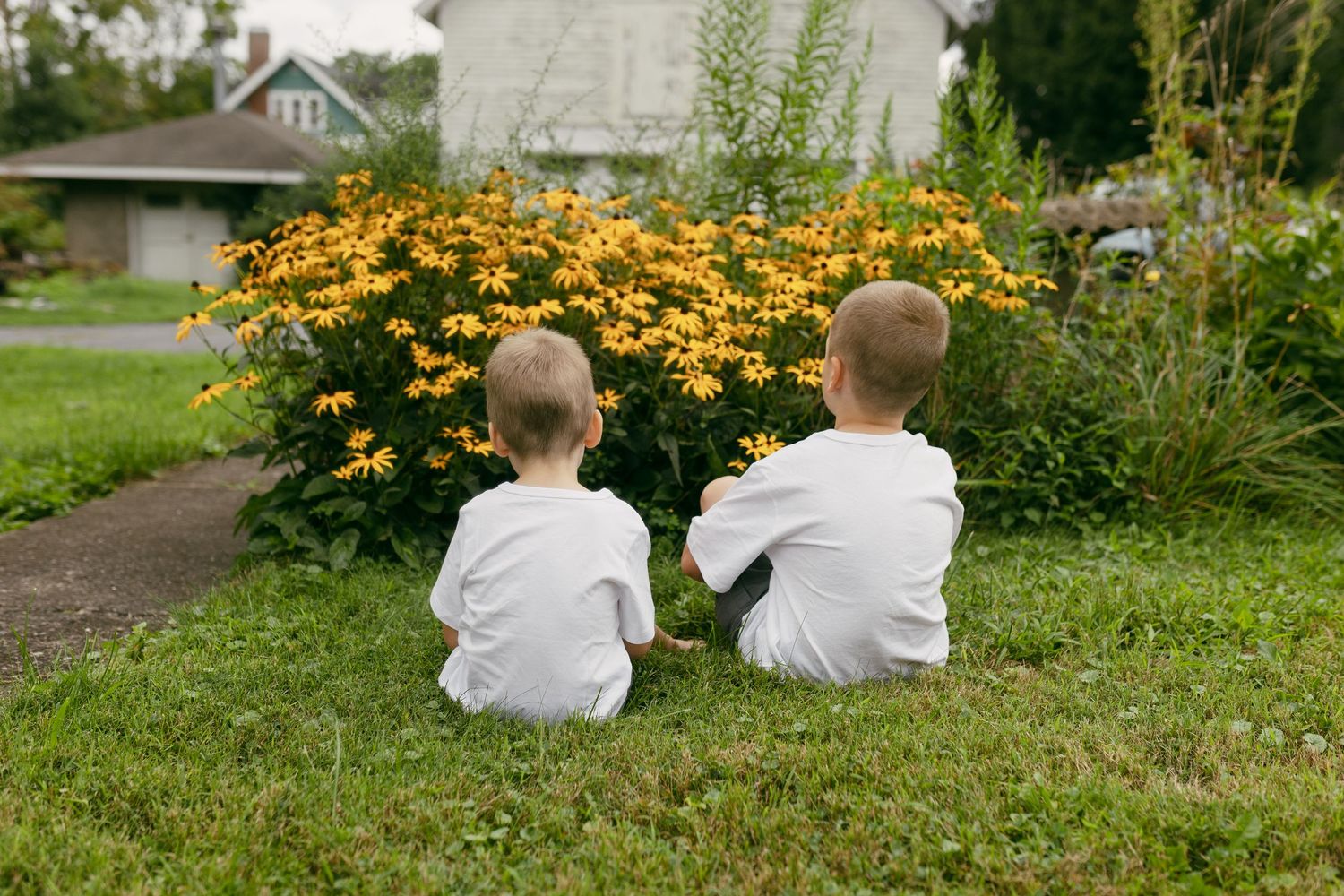 Two children in matching outfits sitting together among blooming yellow flowers.