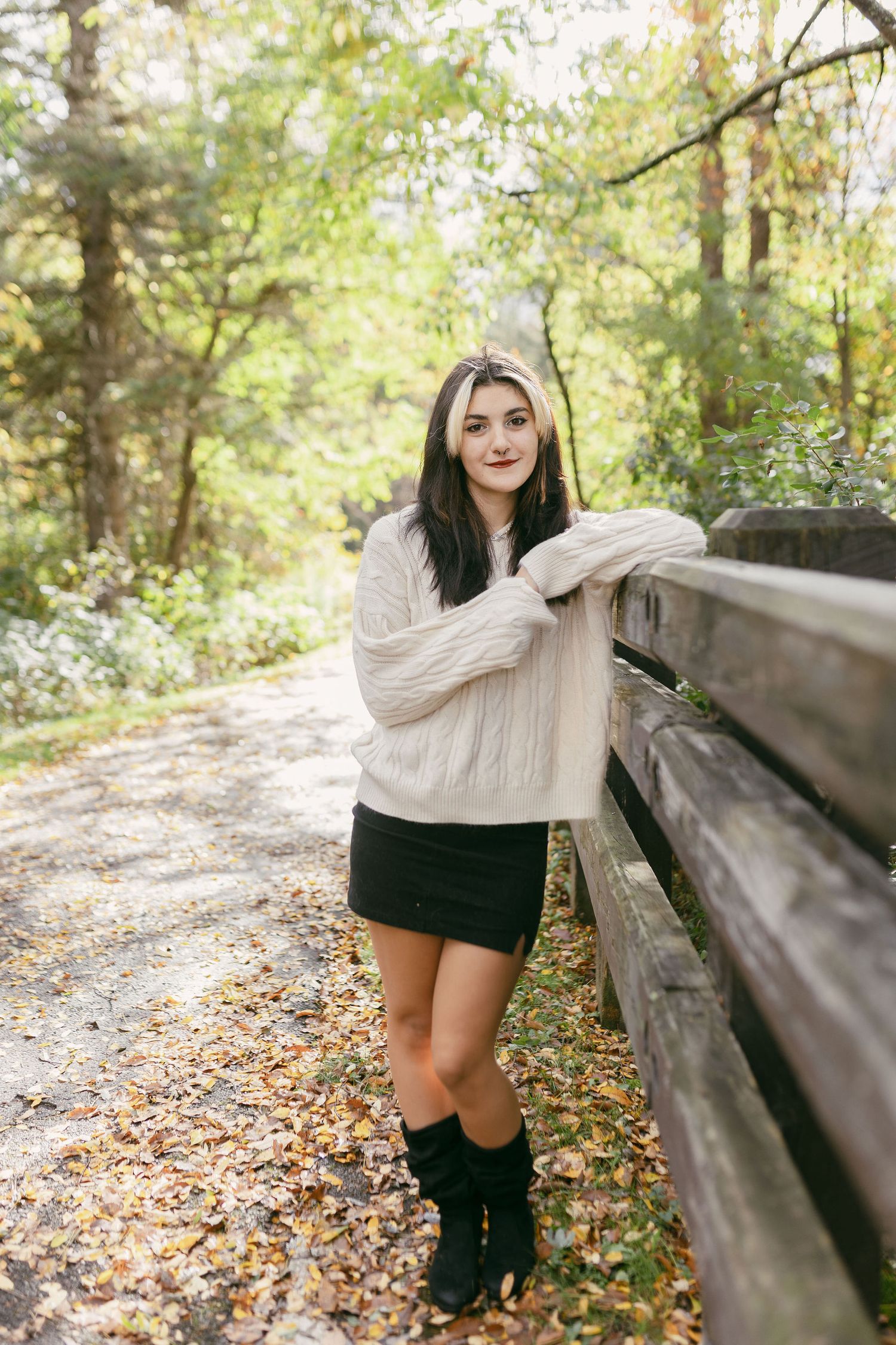 Fall fashion portraits with cream sweater and black skirt against wooden fence and autumn leaves.