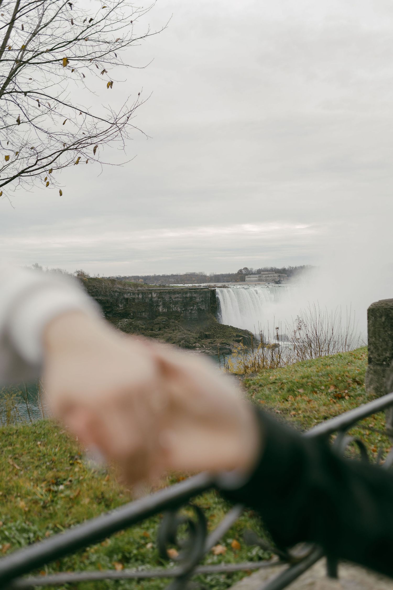 Two hands holding near Niagara Falls on a cloudy autumn day, with mist rising from the waterfall in the background.