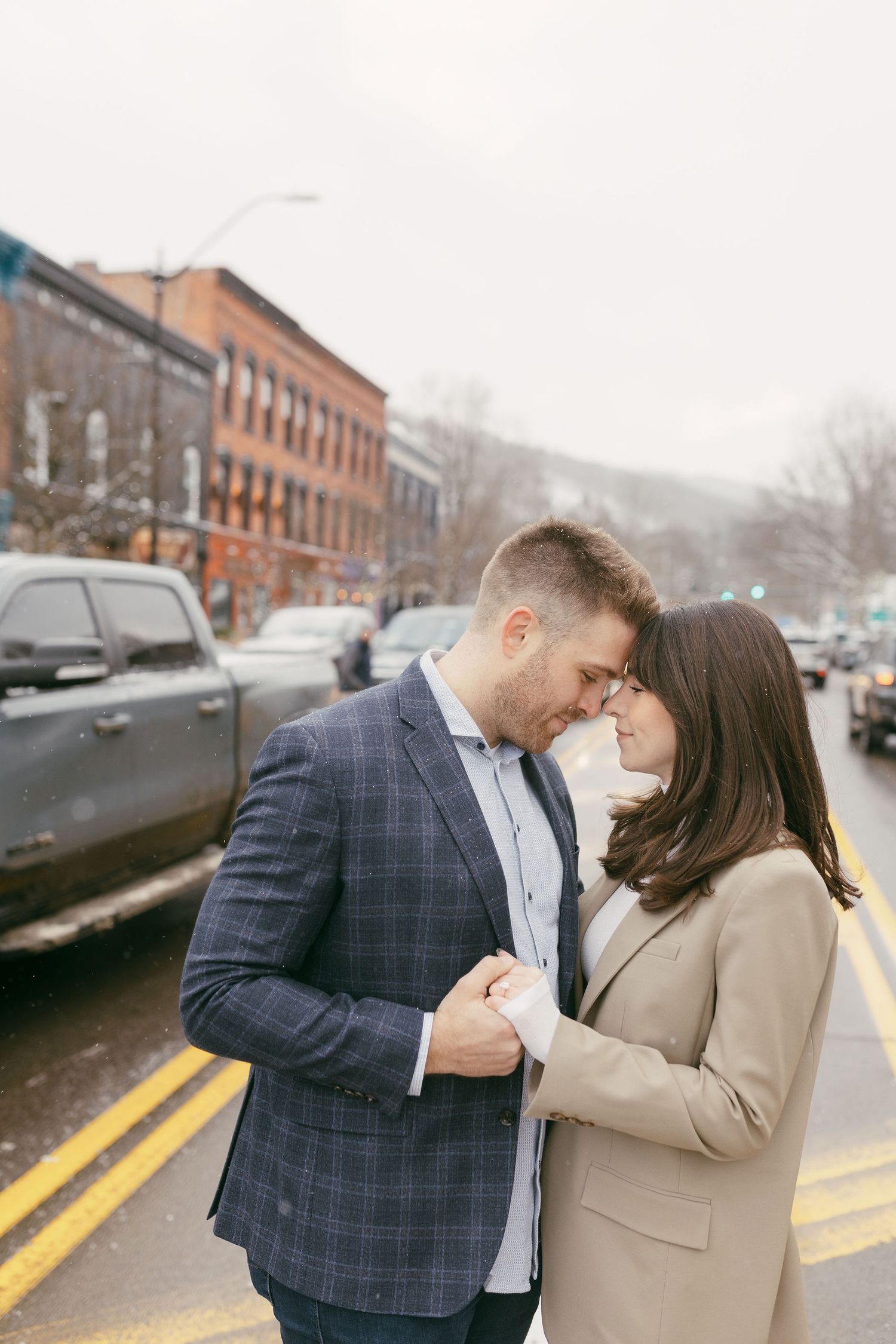 Engaged couple holding hands and touching foreheads on a city street in winter.