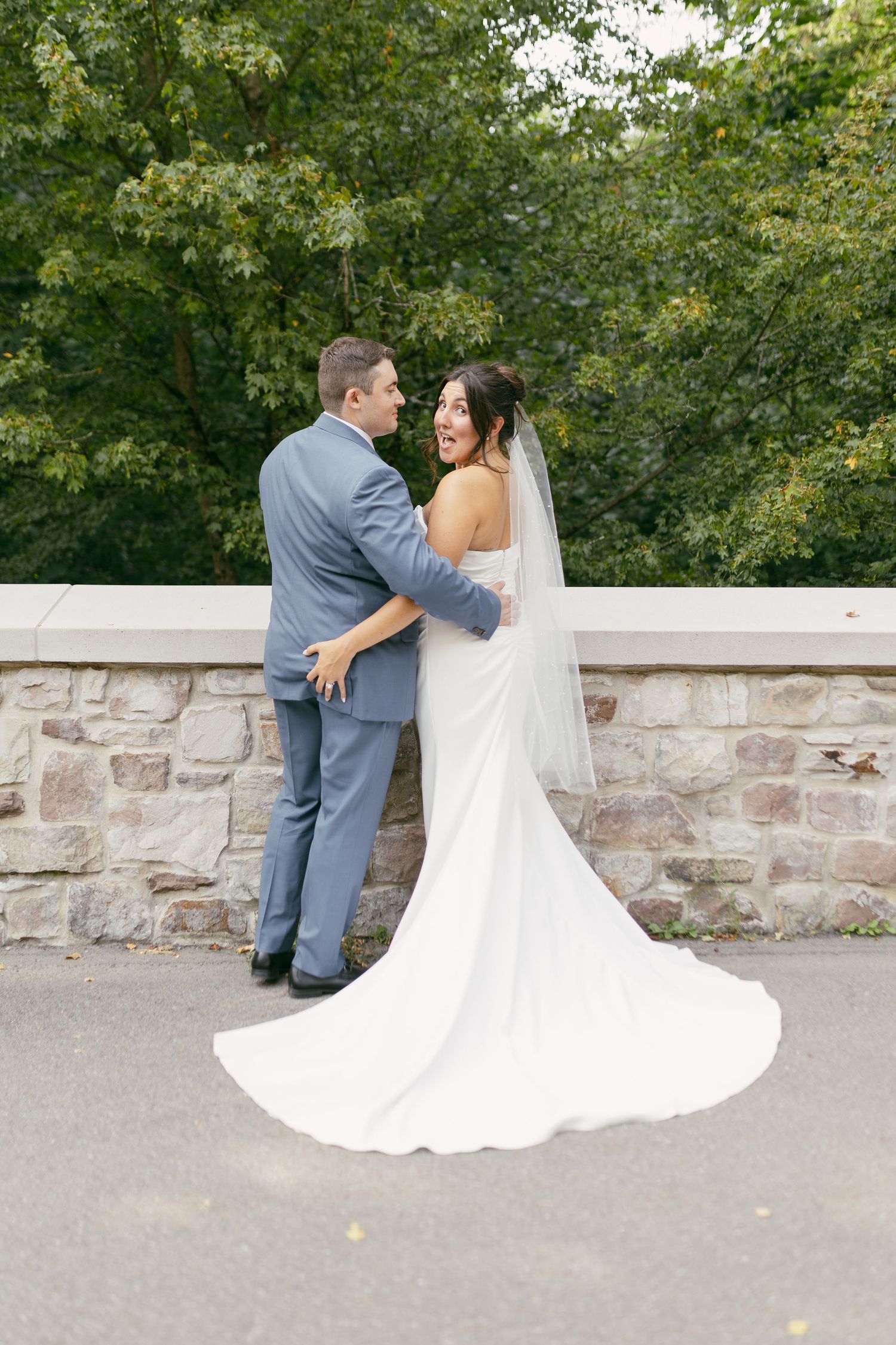 Couple shares a joyful moment against a stone wall backdrop in their wedding attire.
