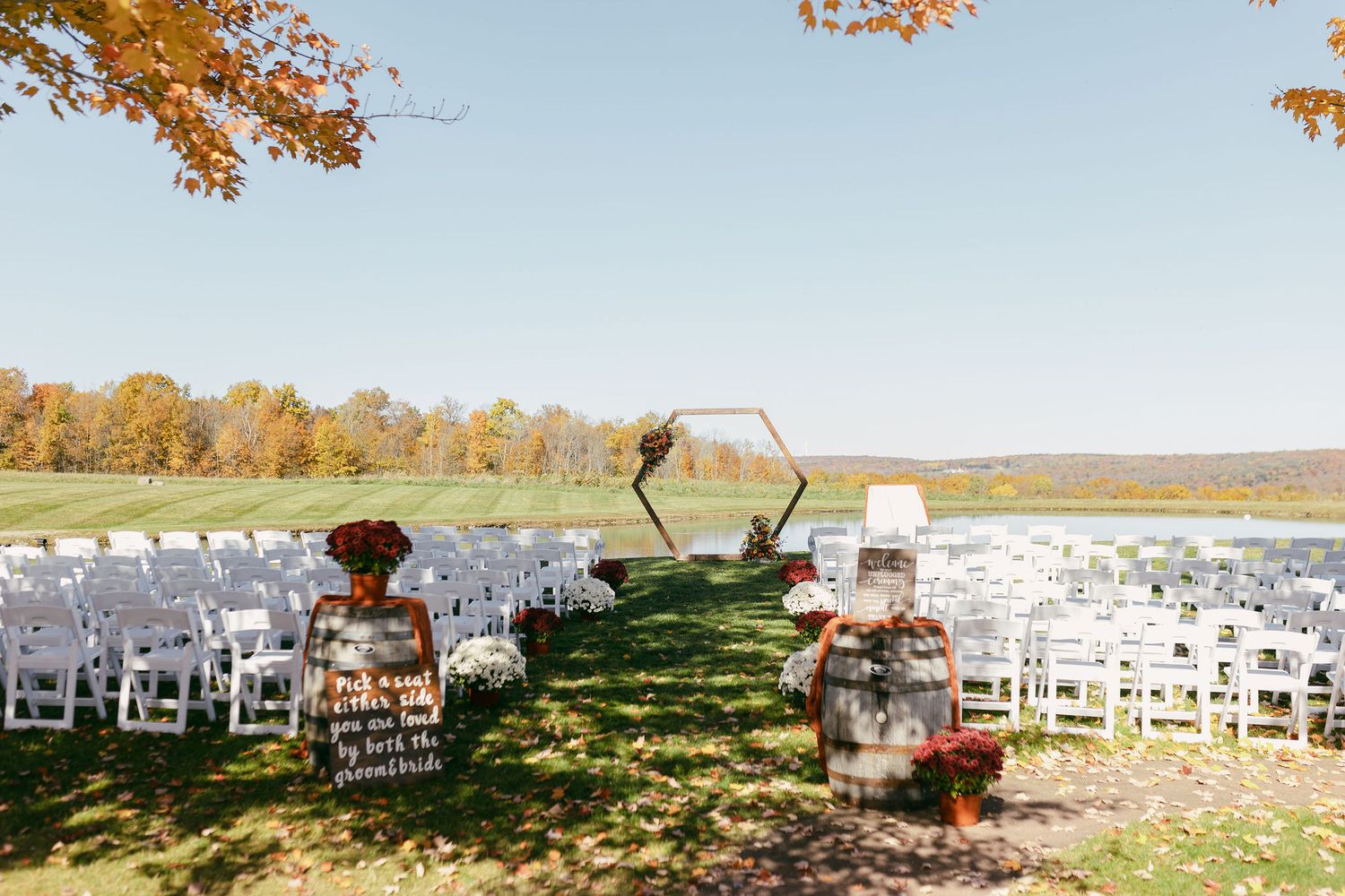 Outdoor wedding ceremony setup with white chairs arranged on a hilltop during peak fall foliage.