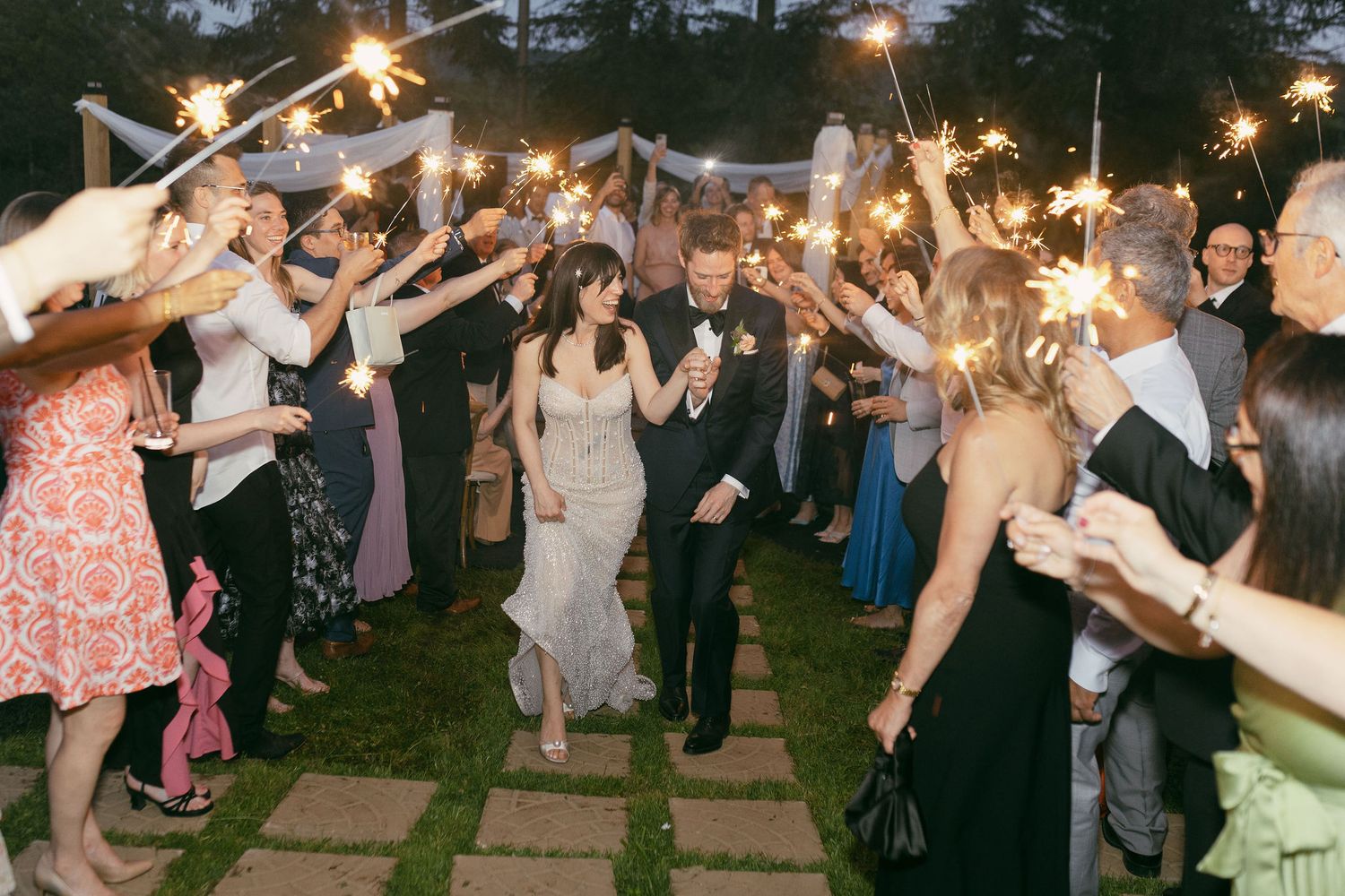 Wedding guests celebrate with sparklers during evening outdoor reception.