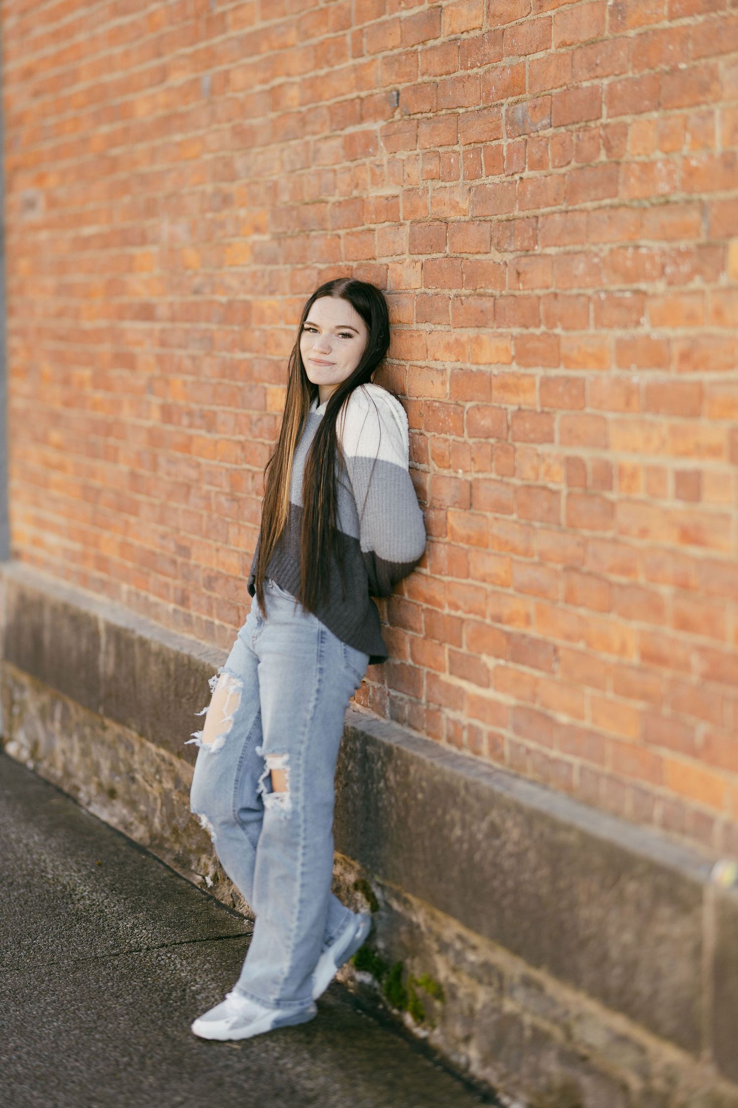 Casual pose against rustic brick wall wearing denim and gray sweater.