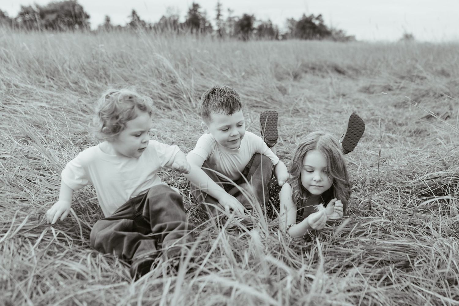 Three children playing together in a tall grass field, captured in a nostalgic black and white photograph.