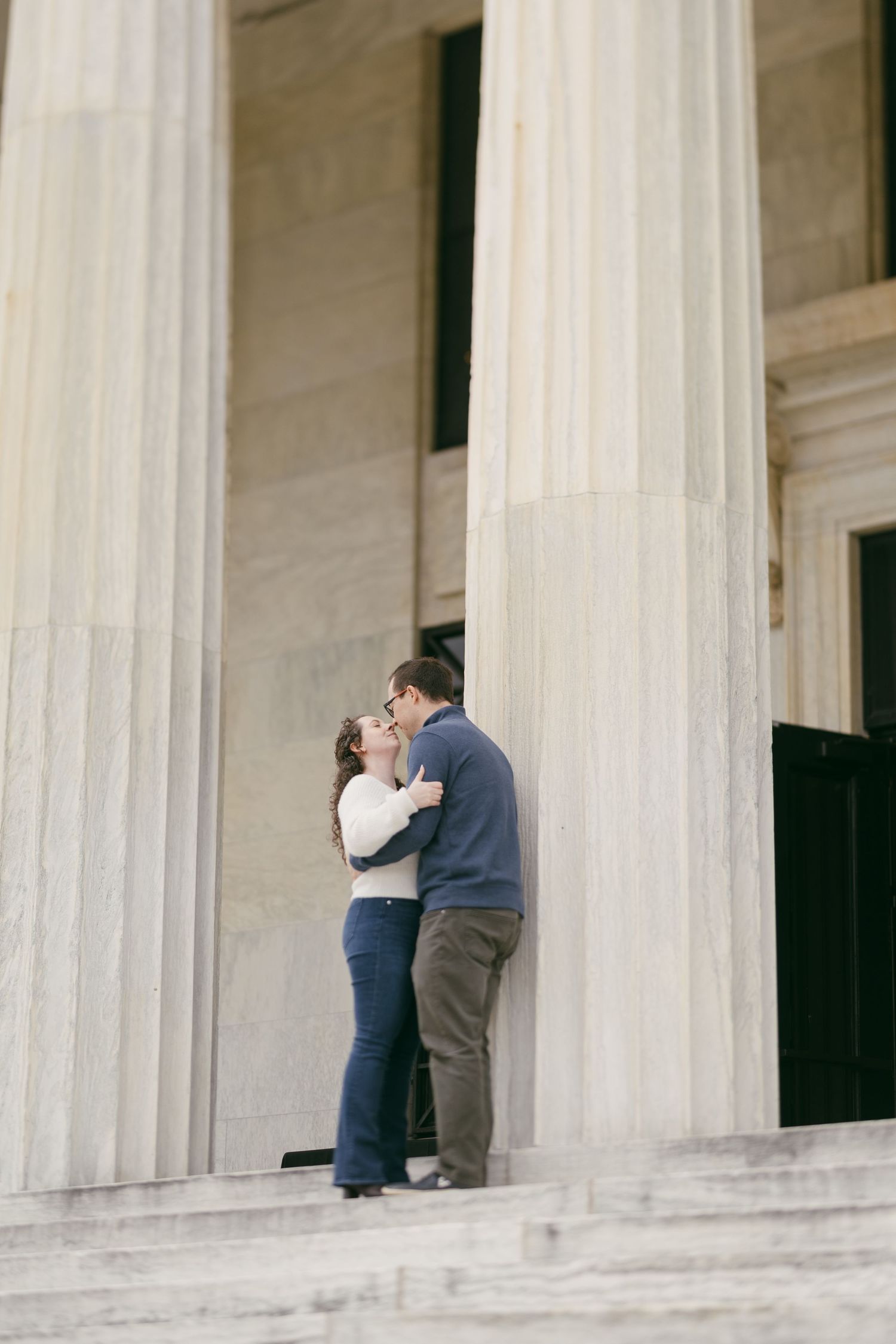 Couple sharing a romantic kiss on the steps of a grand neoclassical building with tall white columns.
