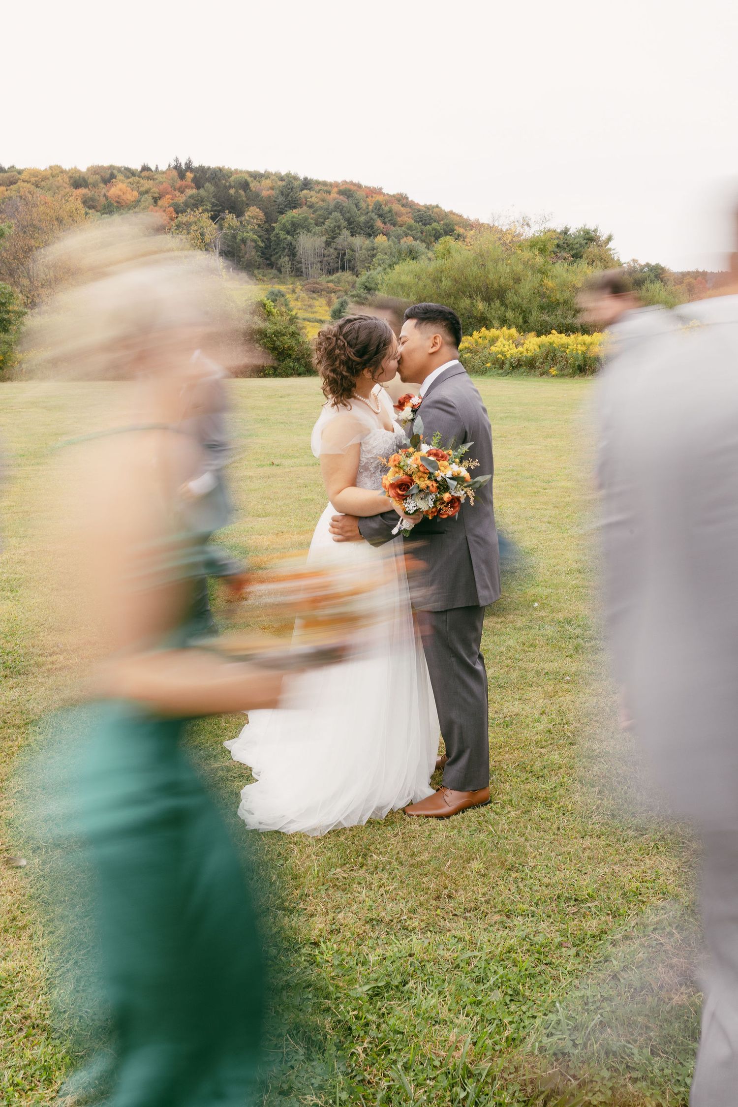 Wedding ceremony taking place on a grassy hillside with motion blur of guests walking past.