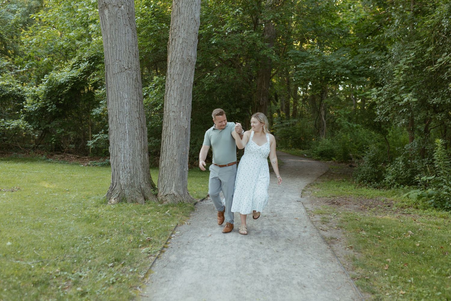 Couple walking hand in hand on a garden path surrounded by lush green trees.