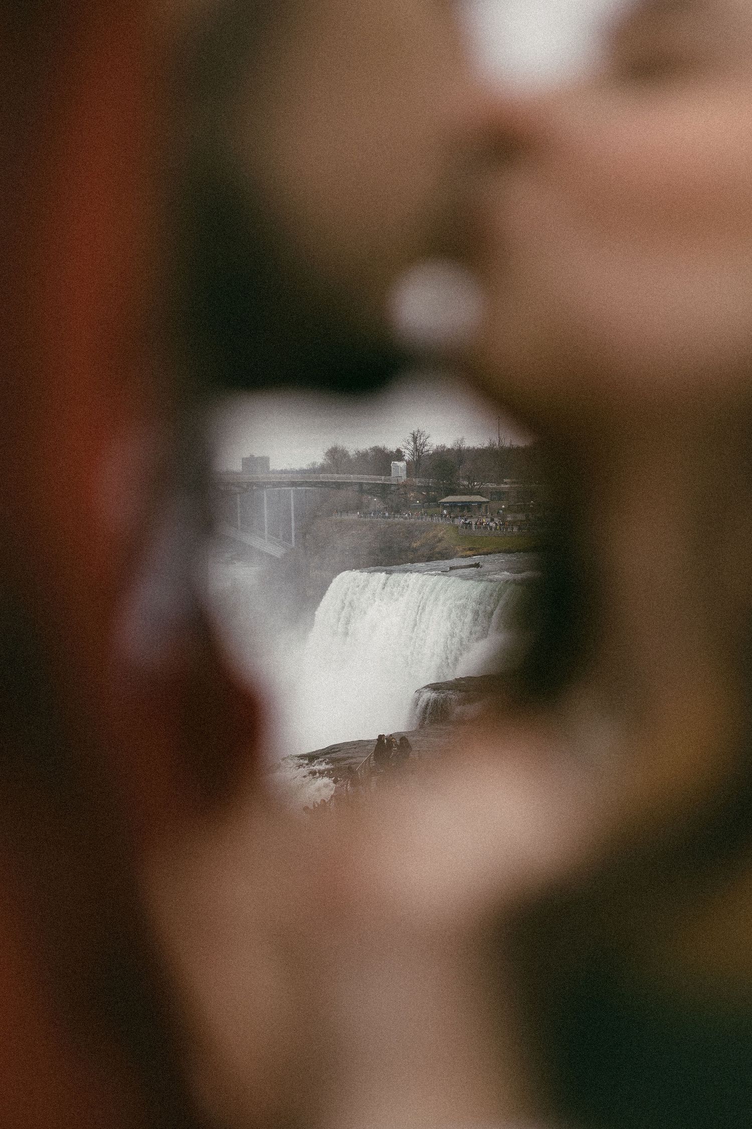 Couple kissing with Niagara Falls visible between them in a creative blurred foreground shot.