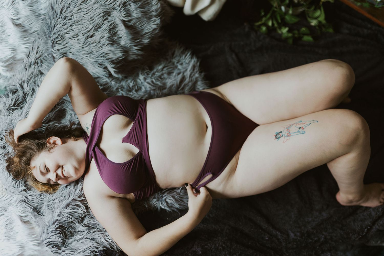 Boudoir photography featuring woman in purple lingerie on grey fur backdrop.