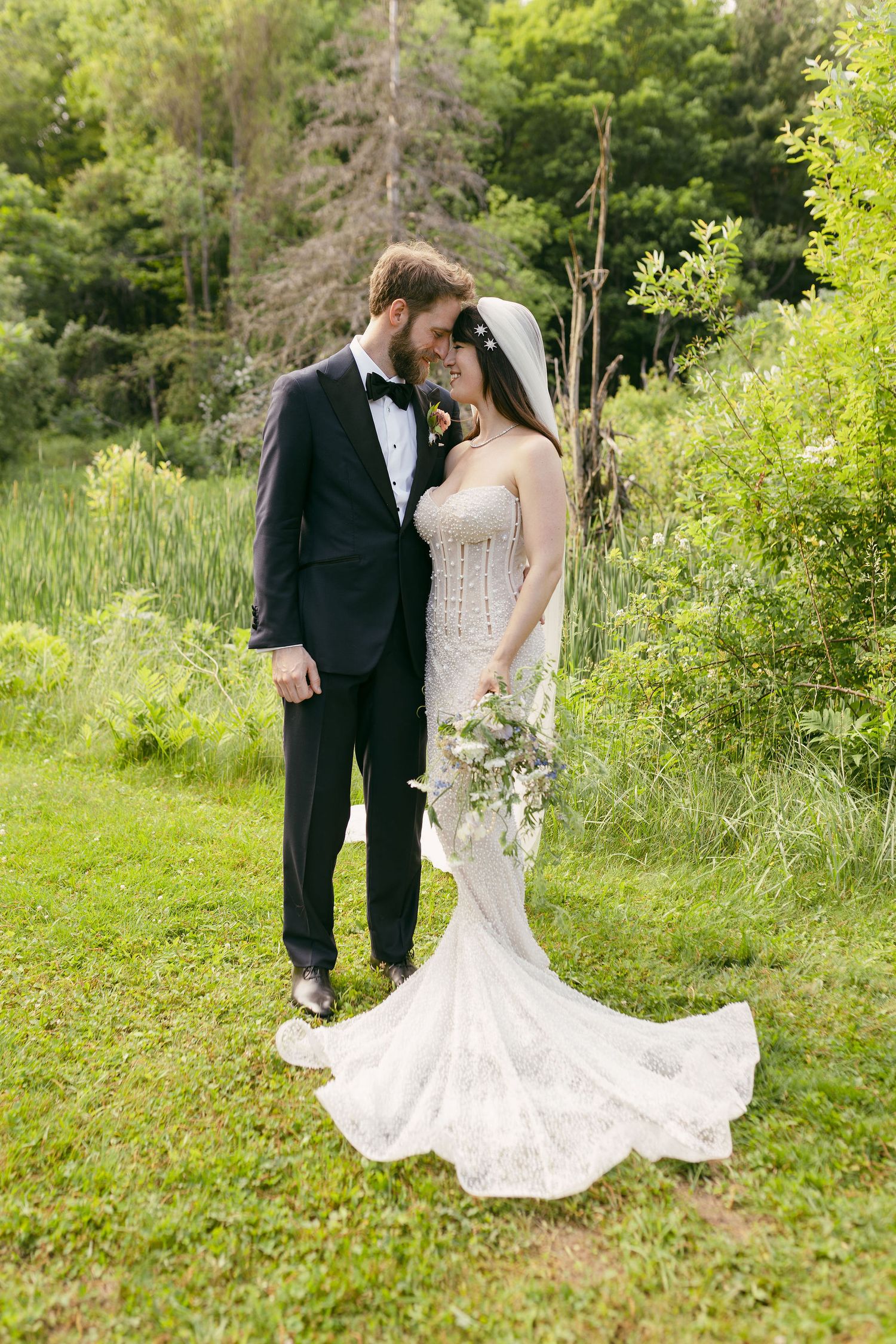 Elegant couple in wedding attire pose together in a lush garden setting.