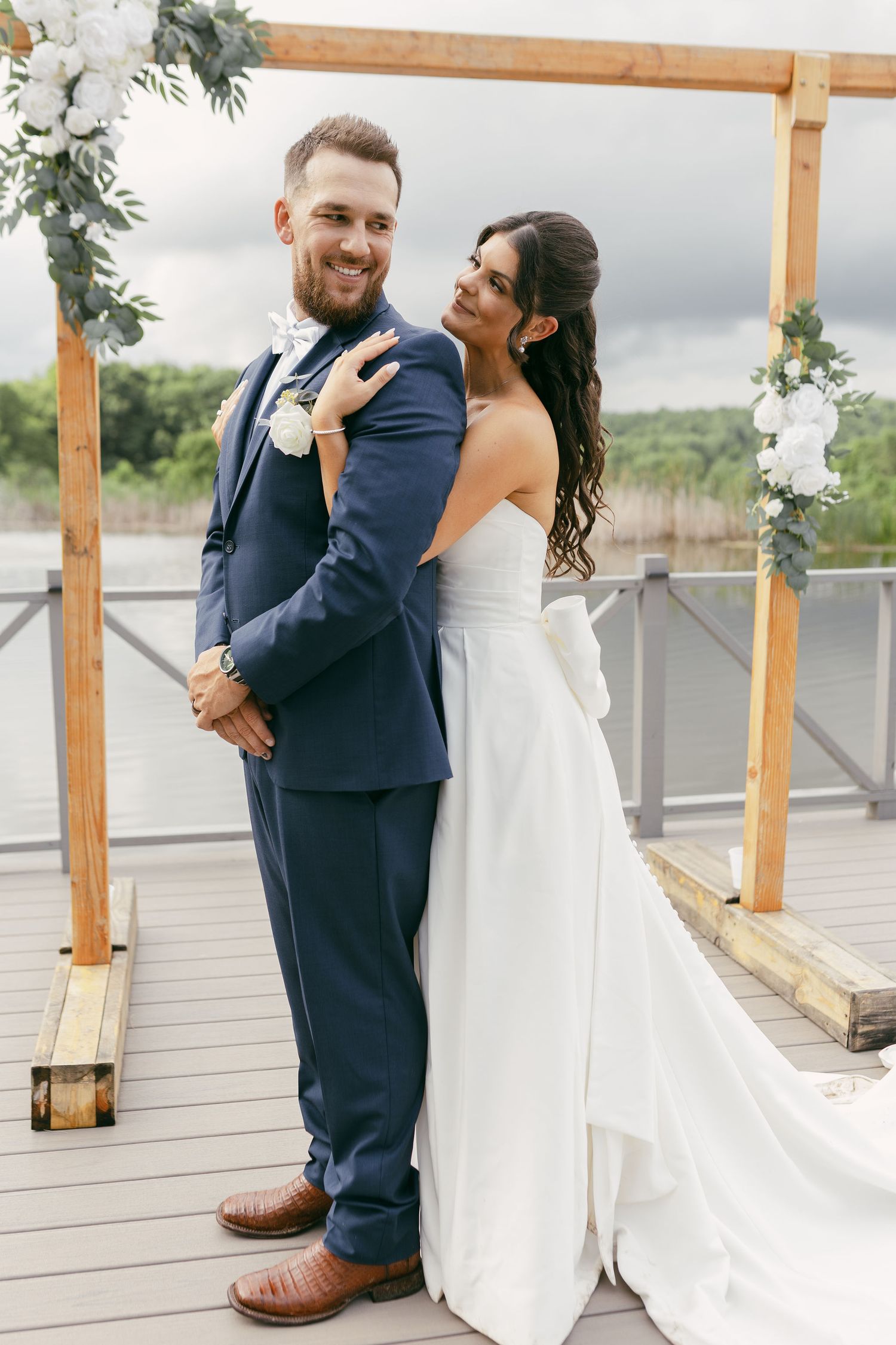 Intimate wedding moment shared under rustic wooden pergola with water view.