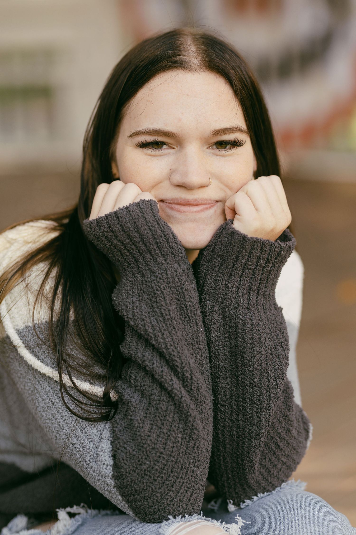 Person wearing a gray sweater covering their face while smiling.