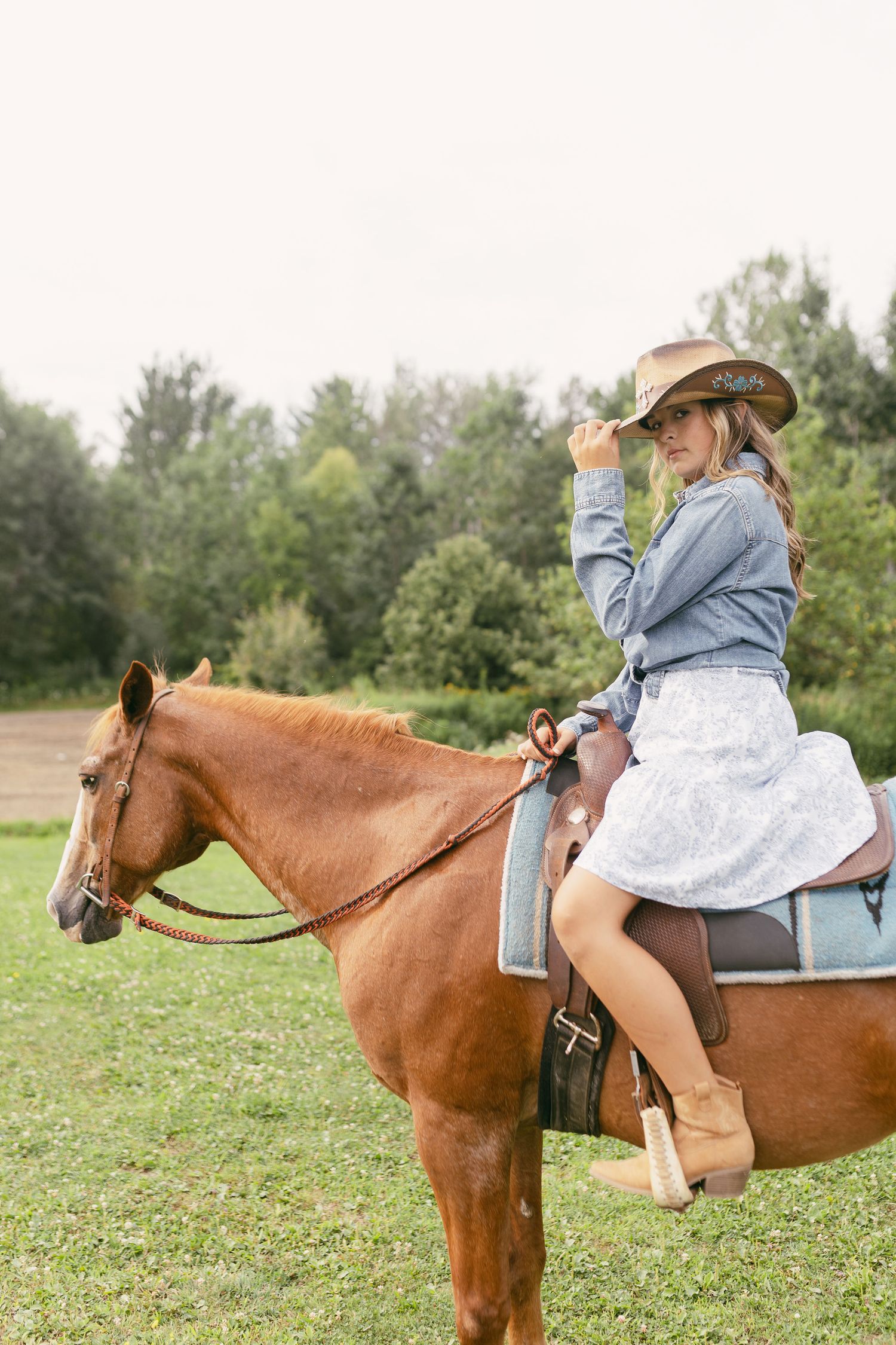 A brown horse with rider wearing denim and boots in an open field.