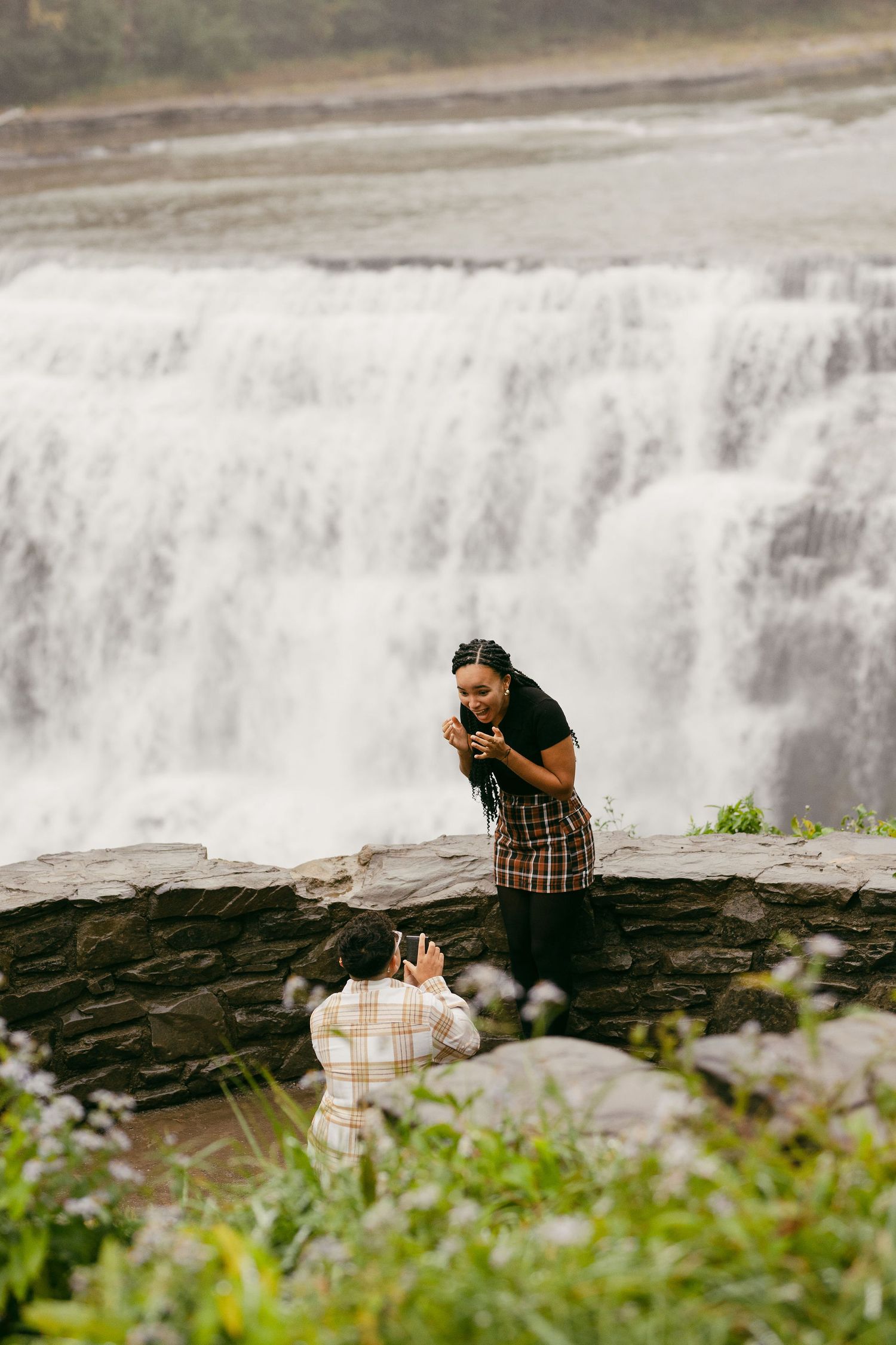 Couple taking photos at the edge of a dramatic waterfall with rocky terrain.