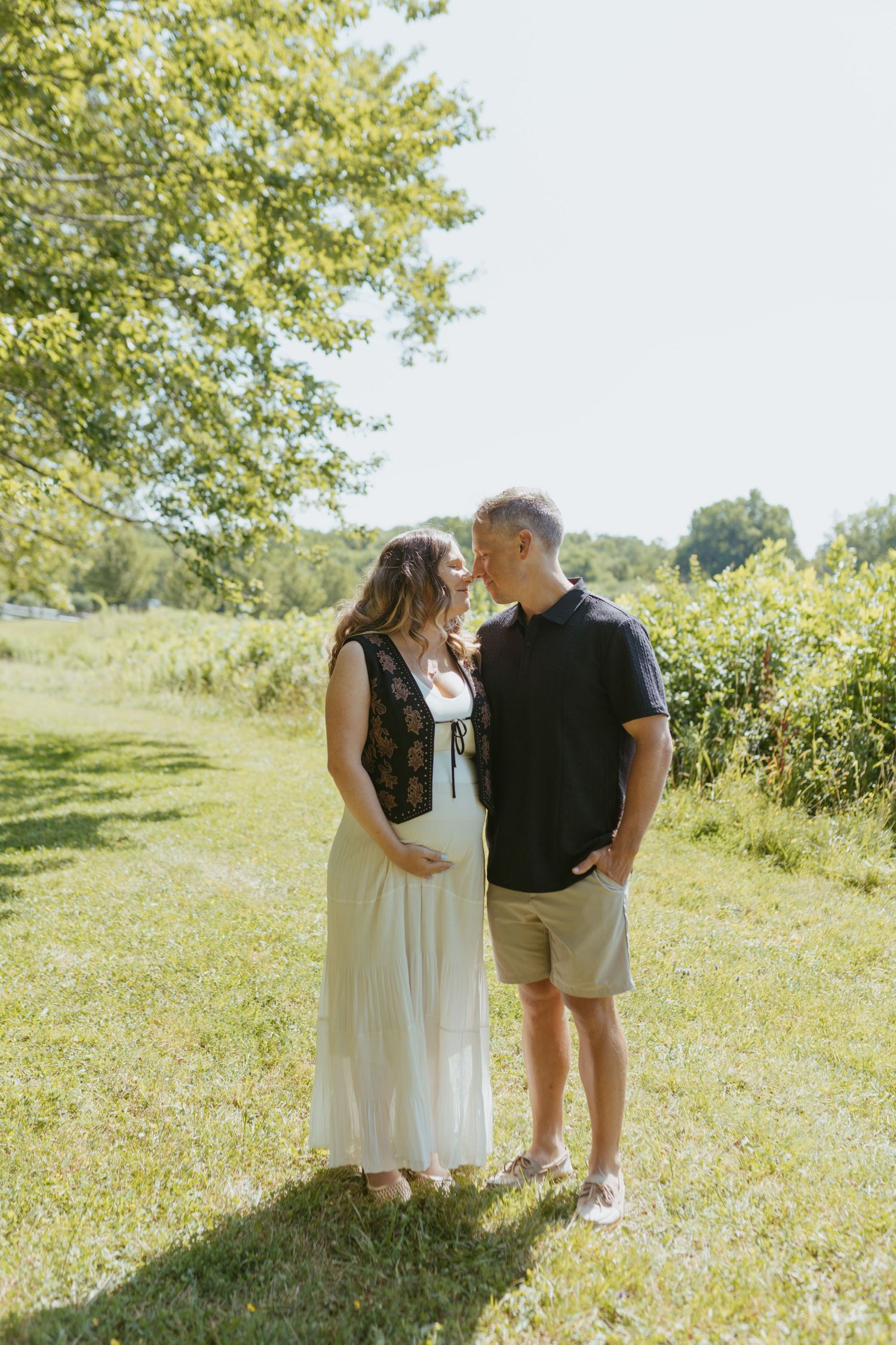 Expecting couple sharing tender moment on sunny green lawn outdoors.