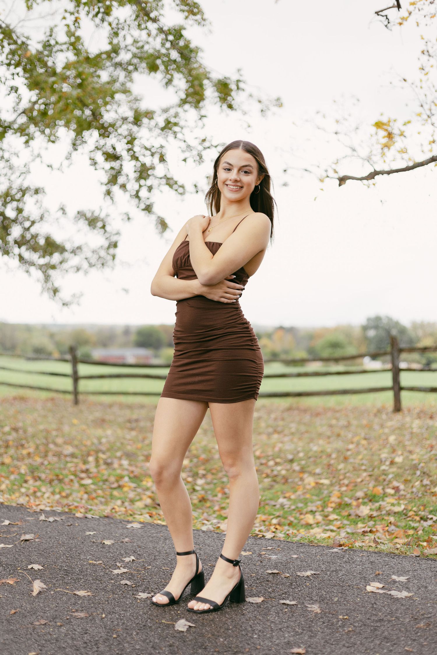 Fashion portrait series showing brown dress and heels against autumn backdrop with fallen leaves on pavement.