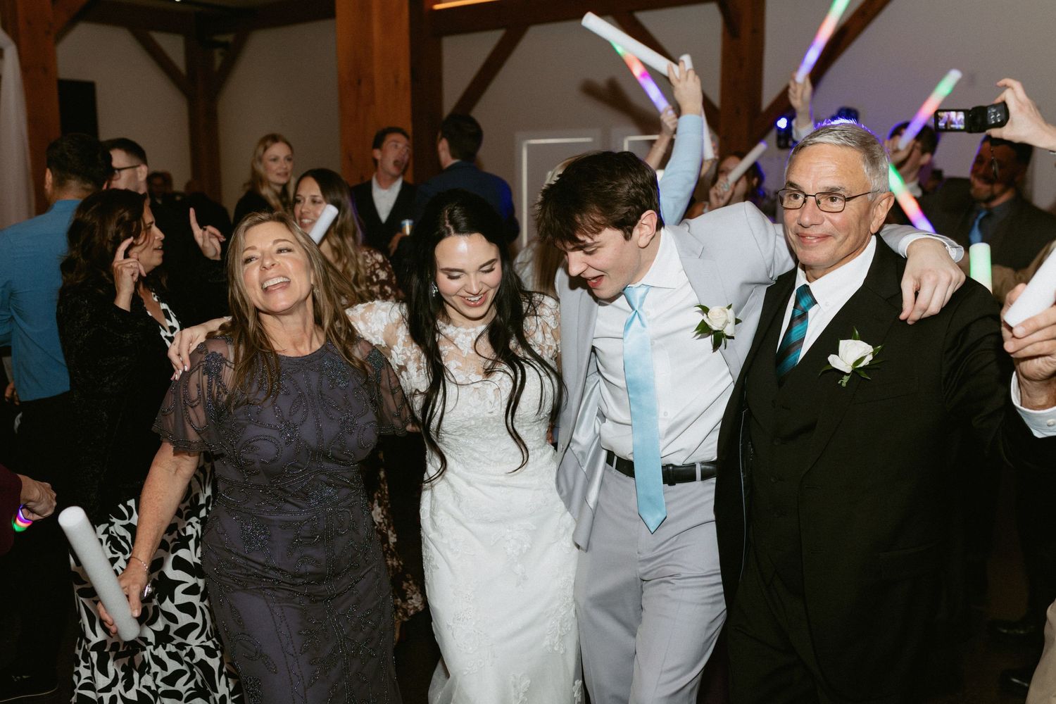 Wedding party dancing with glowing LED foam sticks during reception celebration.