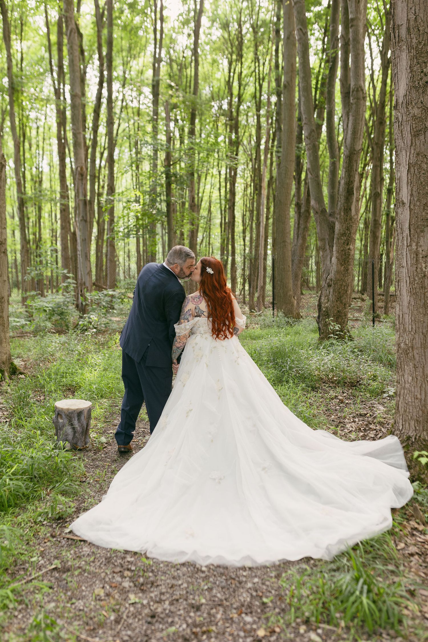Flowing white wedding dress train spreads beautifully across forest floor.