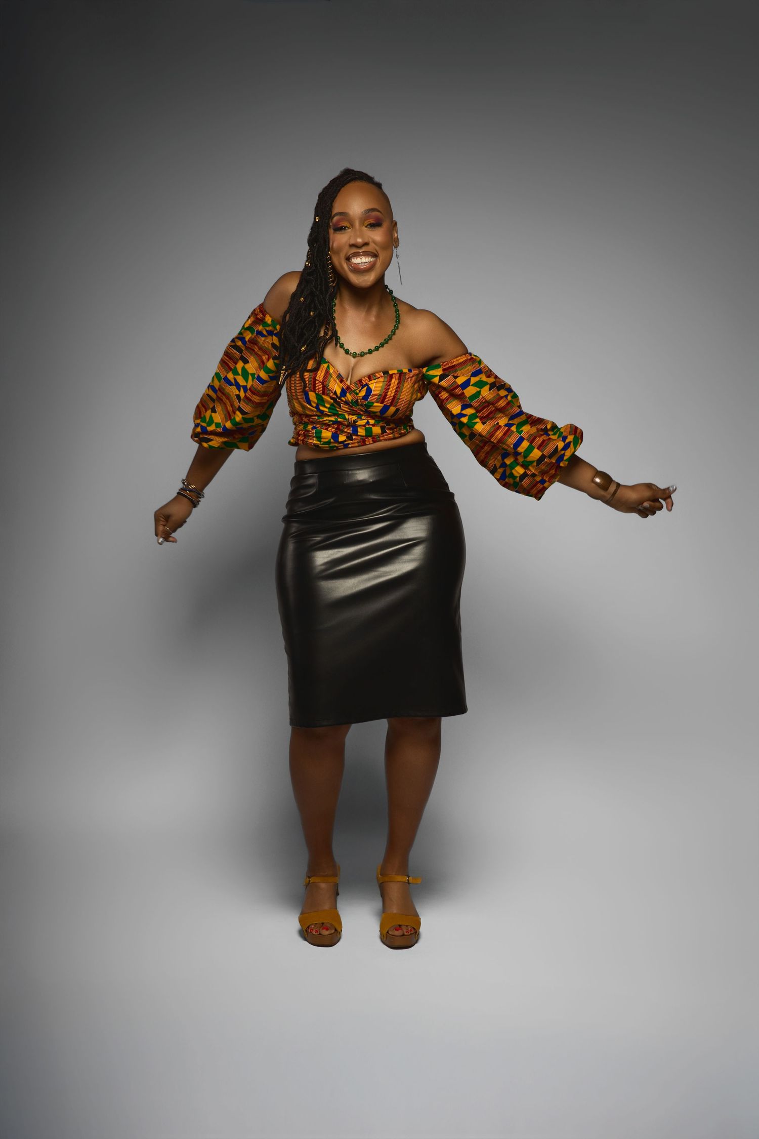 Fashion model wearing colorful African print top and black pencil skirt strikes dynamic pose.