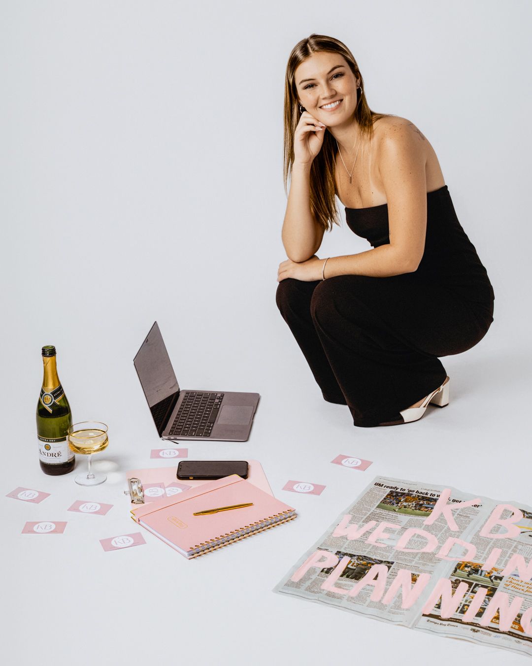 Lifestyle flatlay with laptop, wine bottle, and pink stationery on white background.
