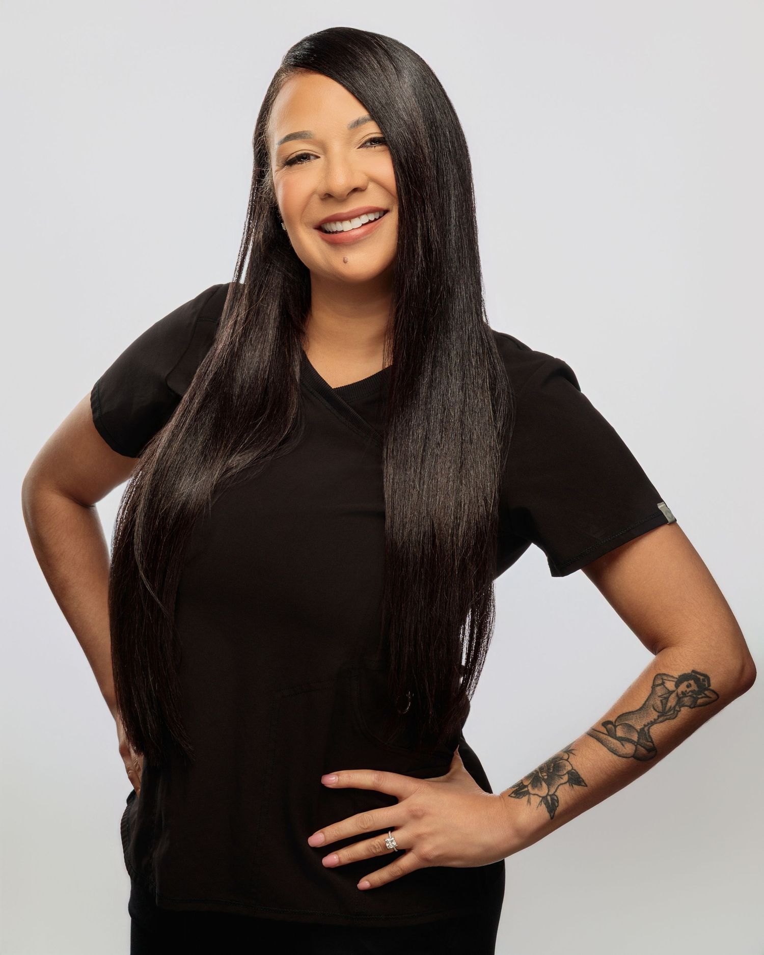 A person with long straight black hair wearing a black shirt poses playfully against a white background.