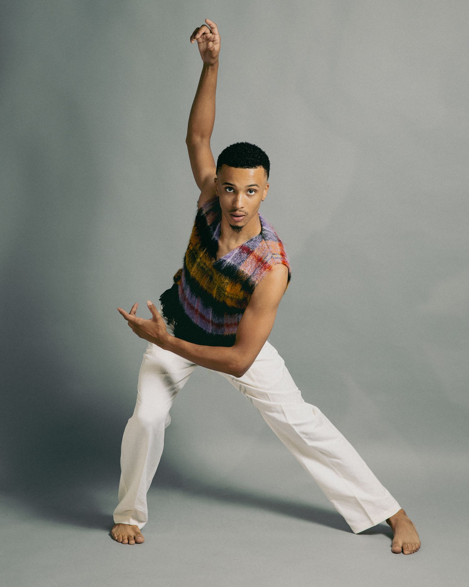 A dancer in white pants performs a dynamic sequence of contemporary dance movements against a gray backdrop.