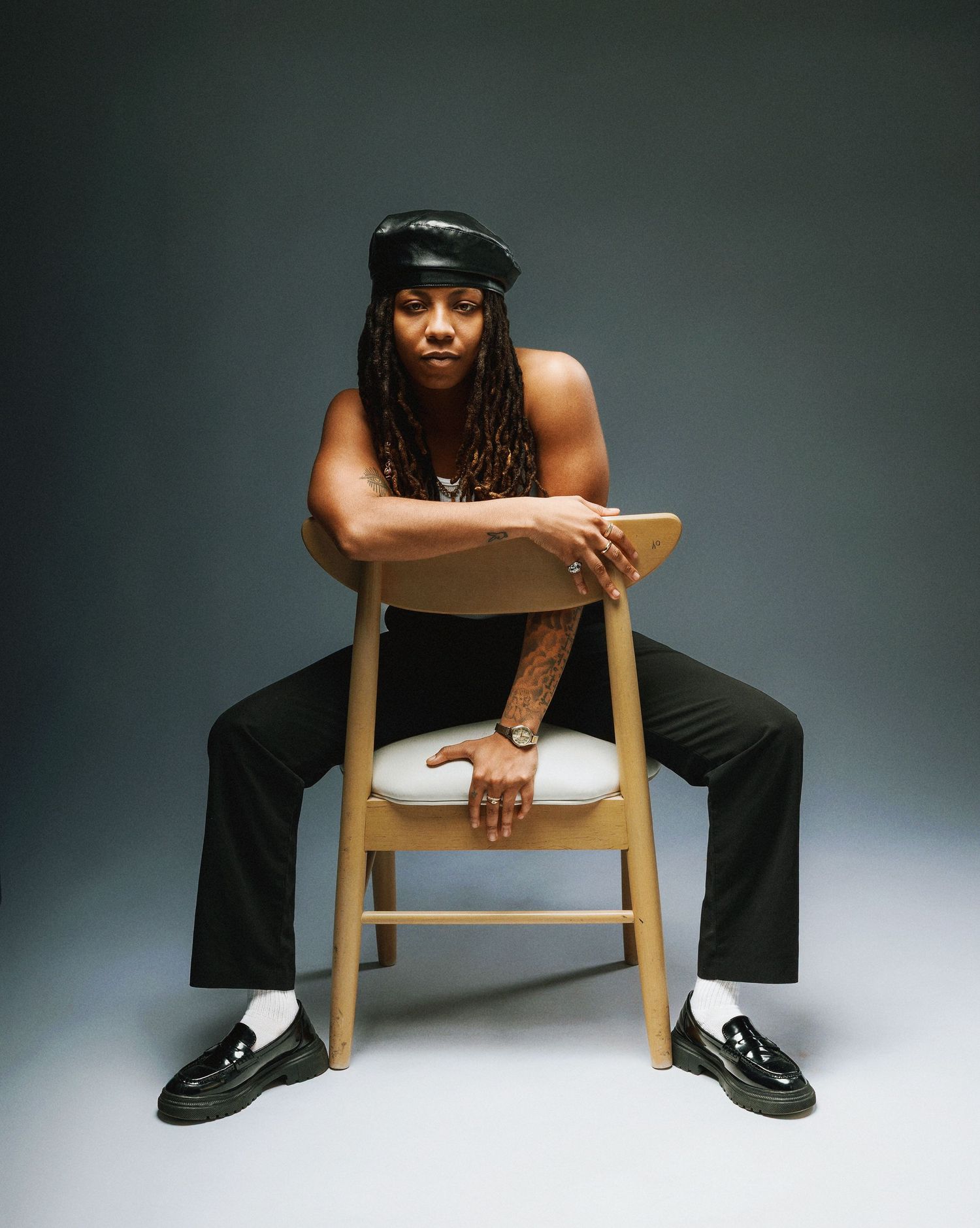 Artistic photo series showing a person in black clothing sitting on a wooden chair in various wide-legged poses against gray backdrop.