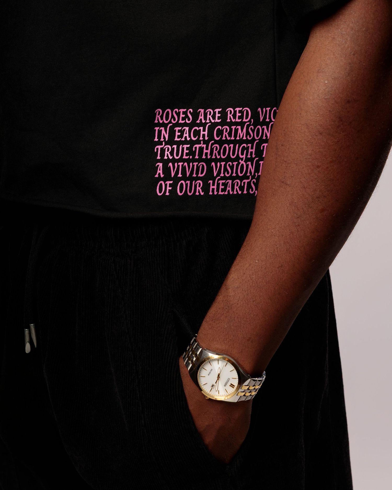 A black garment with pink embroidered text and a watch detail visible in the frame.