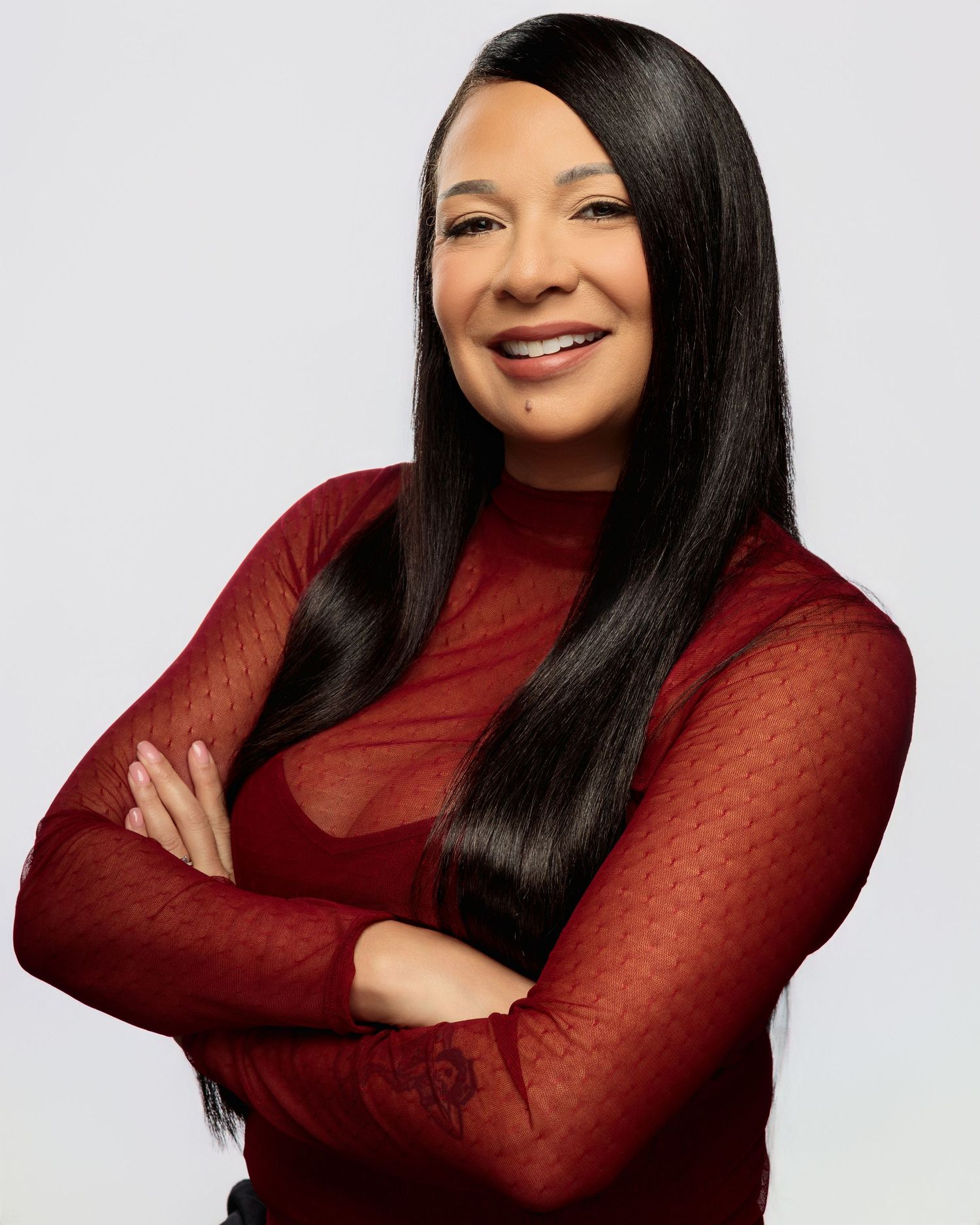 A woman in a burgundy sweater poses against a white background with long black hair and a warm smile.