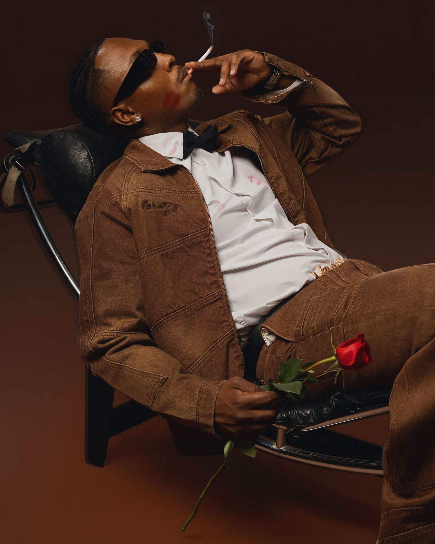 Stylish portrait with red rose showing relaxed pose in brown jacket.
