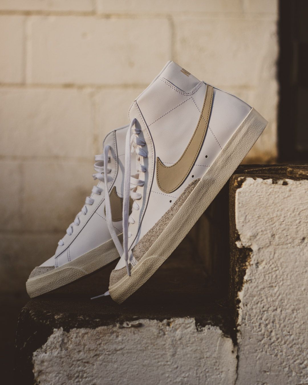 A series of white canvas sneakers balanced on a textured concrete wall in an artistic arrangement.