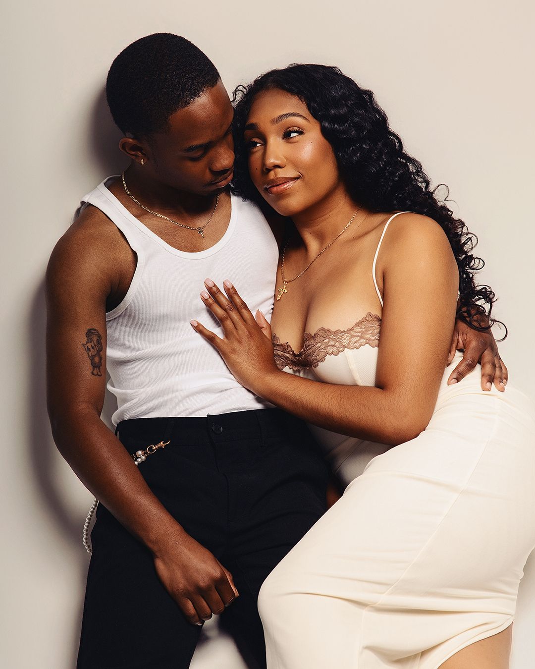 A young couple poses intimately in a studio, wearing white outfits, with soft lighting highlighting their elegant style.