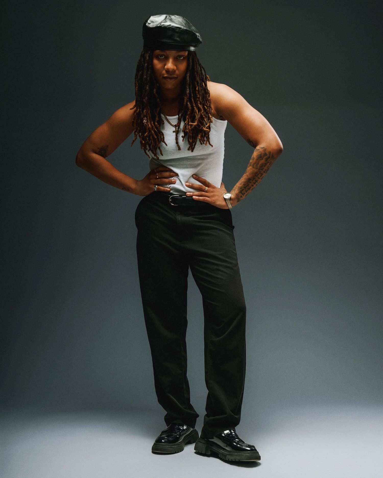 A model crouches while wearing black pants, white top and dark jacket in a professional studio setting.