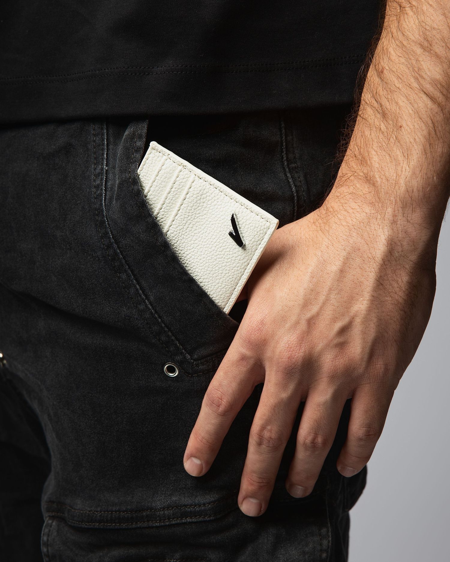 A white leather wallet peeking out of a black denim jeans pocket with a hand resting nearby.