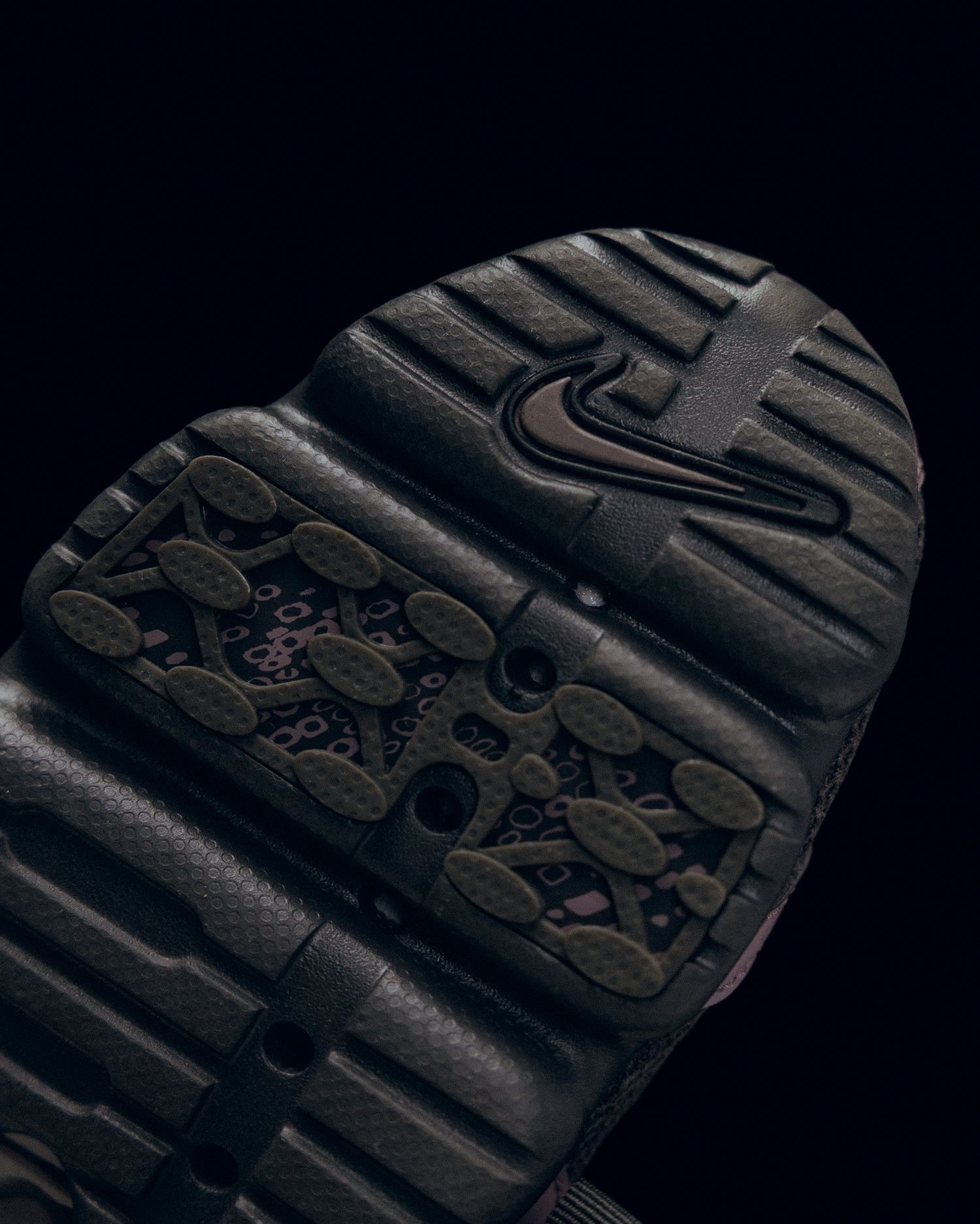 Close-up view of a dark rubber shoe sole with textured Nike swoosh pattern and grip details.