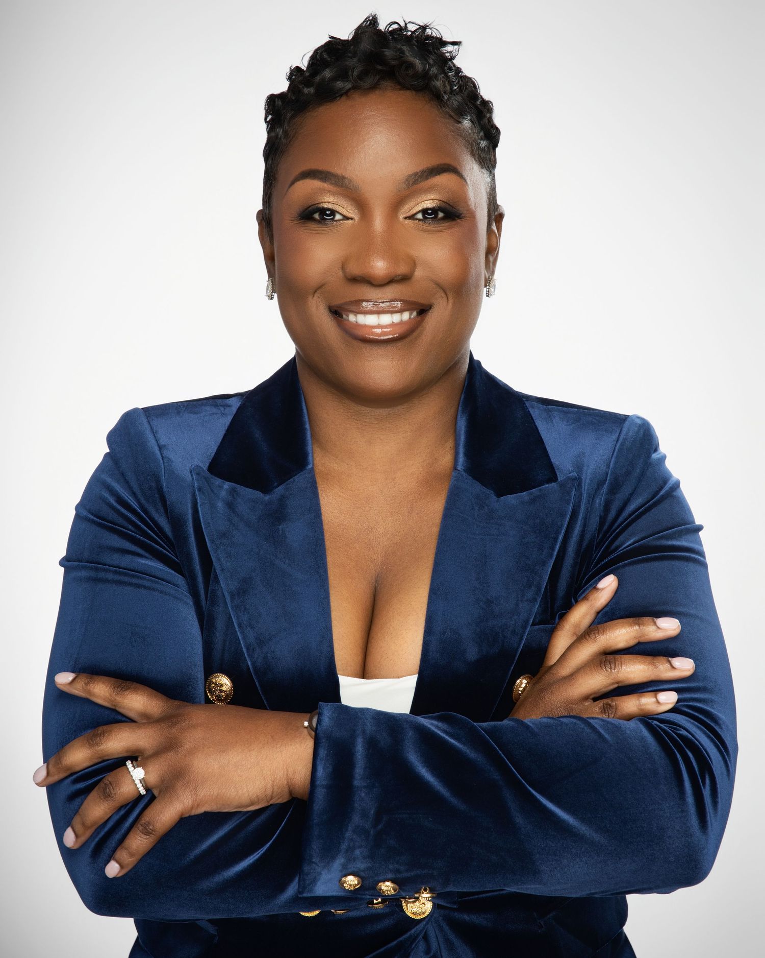 Professional in a navy velvet blazer poses with crossed arms against white background.