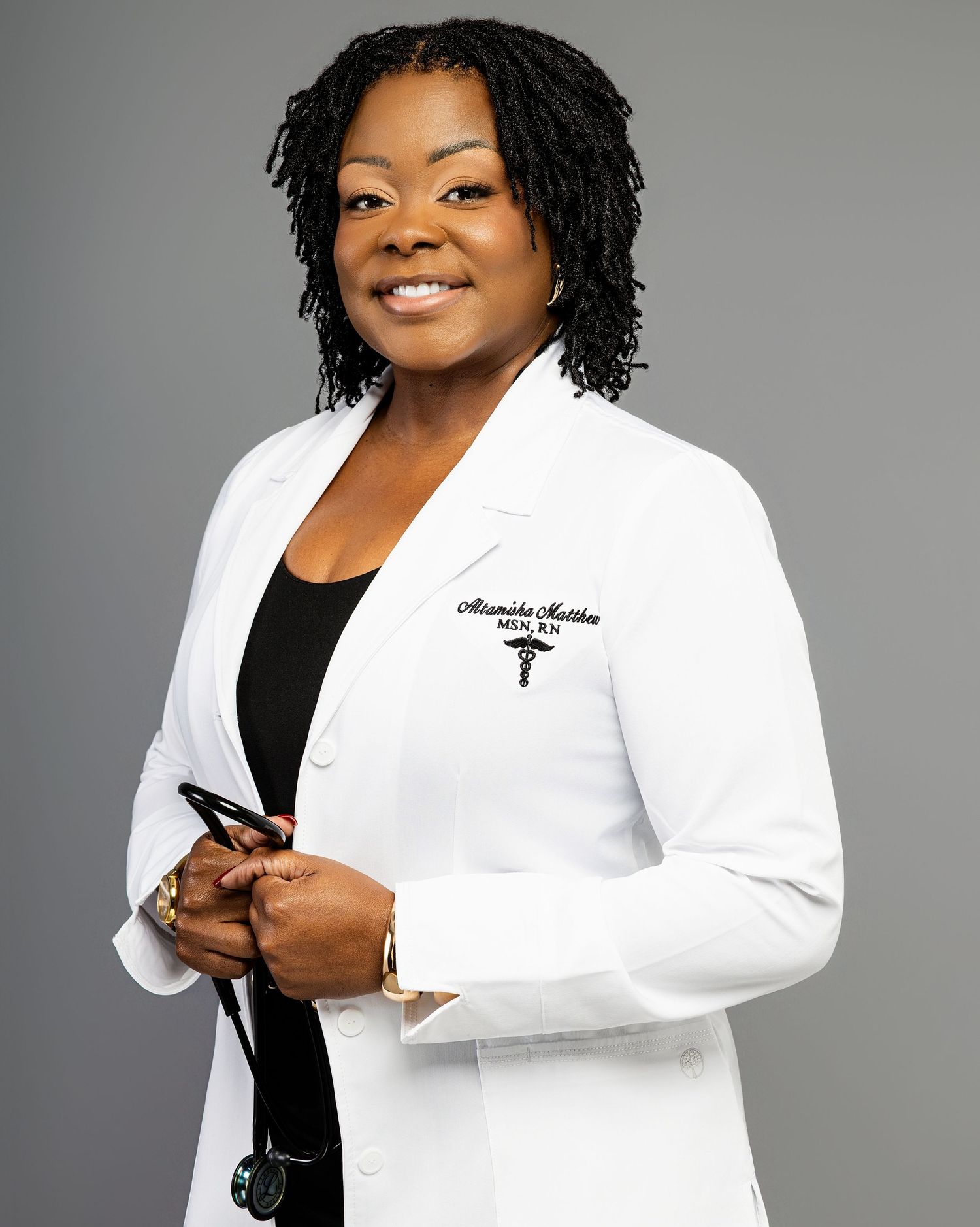 Professional in a crisp white medical coat and black top poses confidently against a gray studio backdrop.
