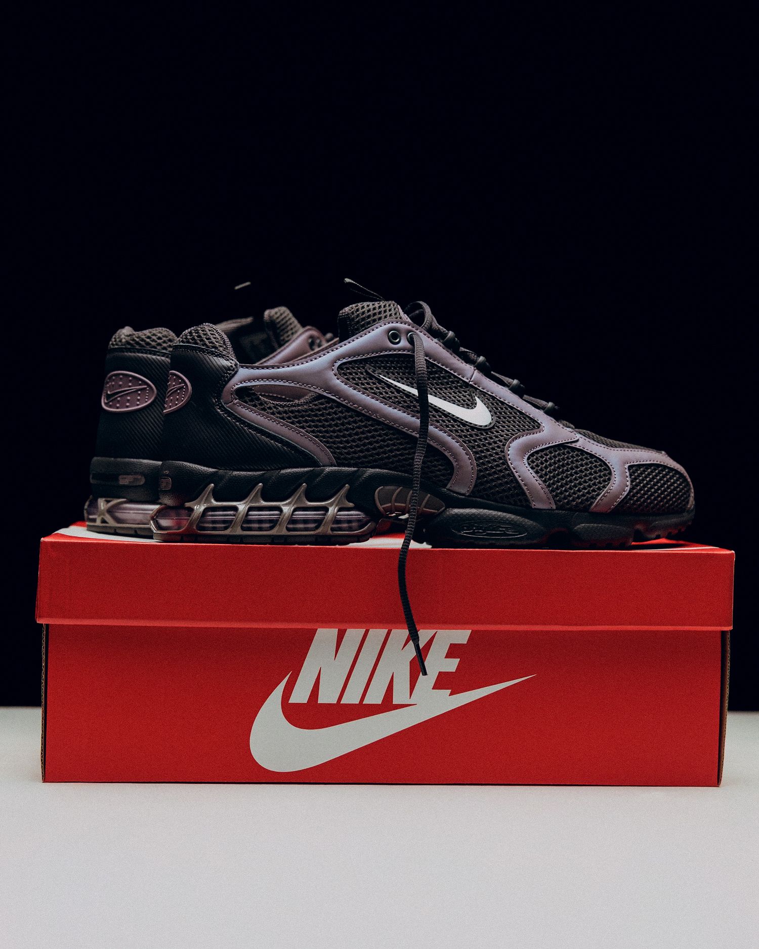Nike sneakers in black and grey colorway displayed on top of a red Nike shoebox against a dark background.