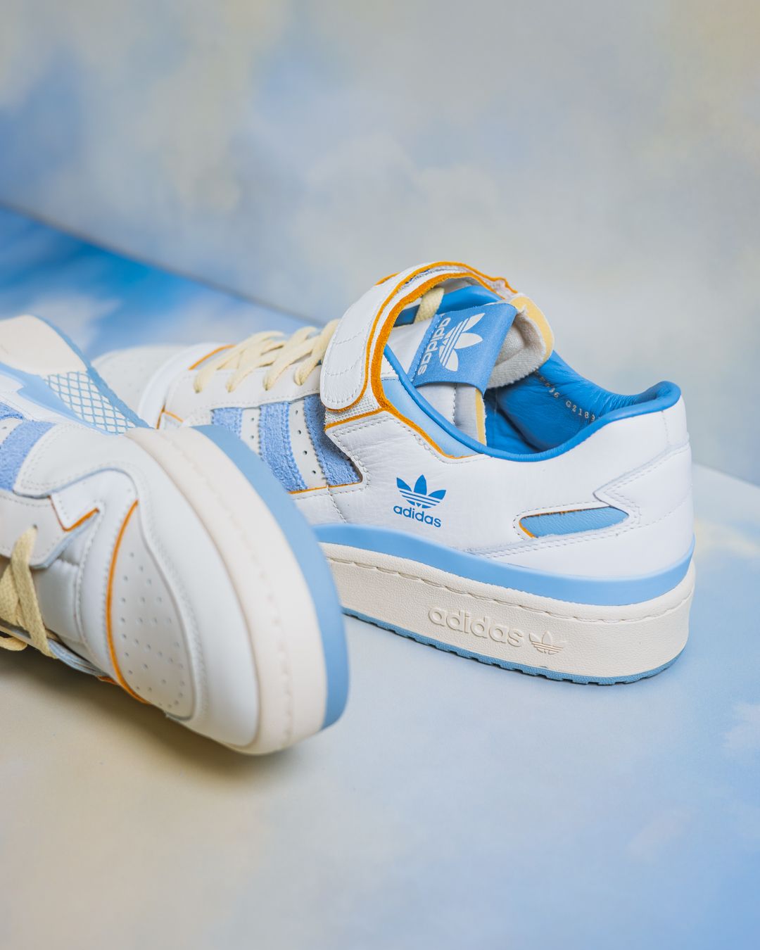 White and blue Adidas Forum sneakers with gold accents photographed against a light background.