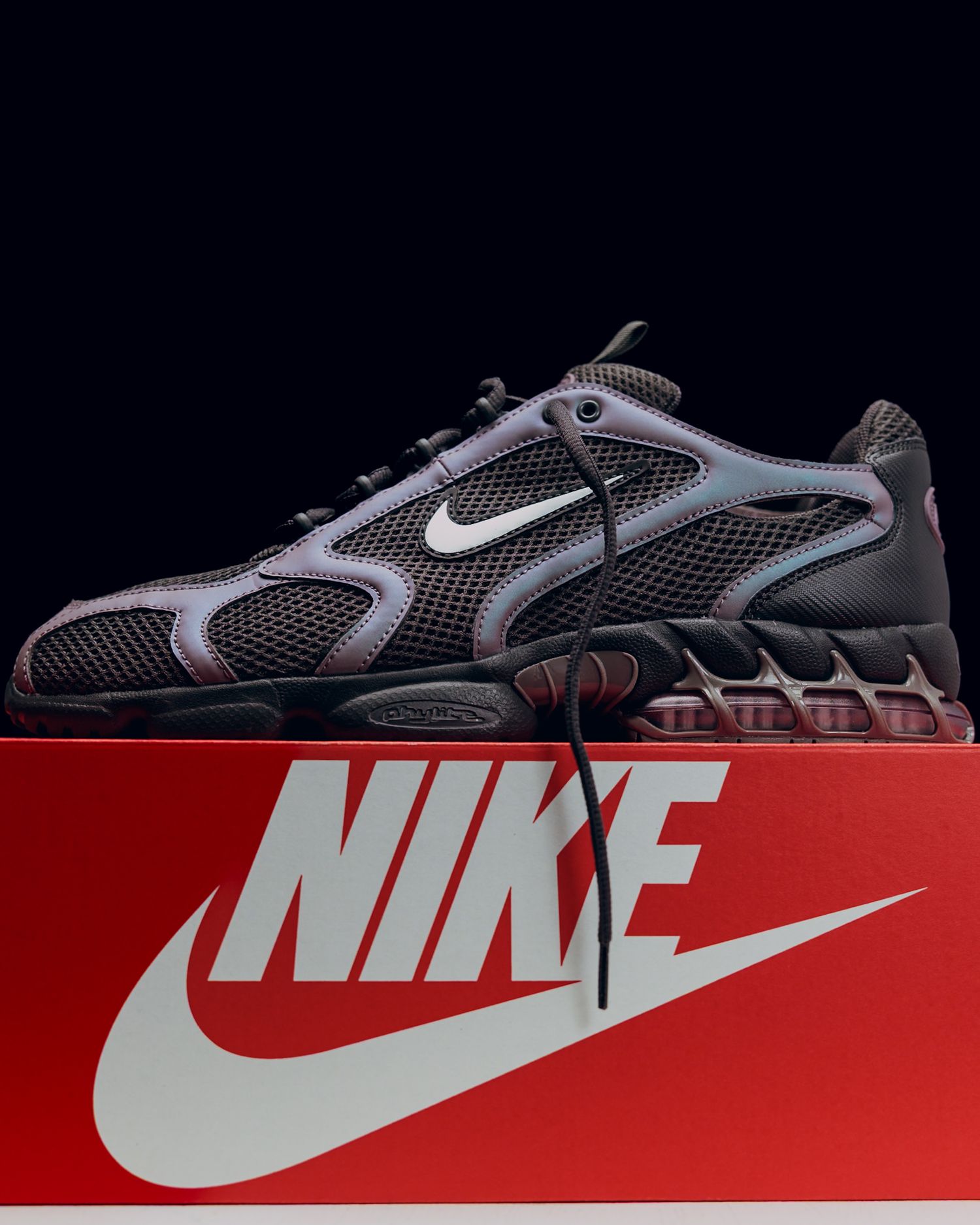 Nike sneaker in gray and black mesh design displayed on a red Nike shoebox with white swoosh logo against dark background.