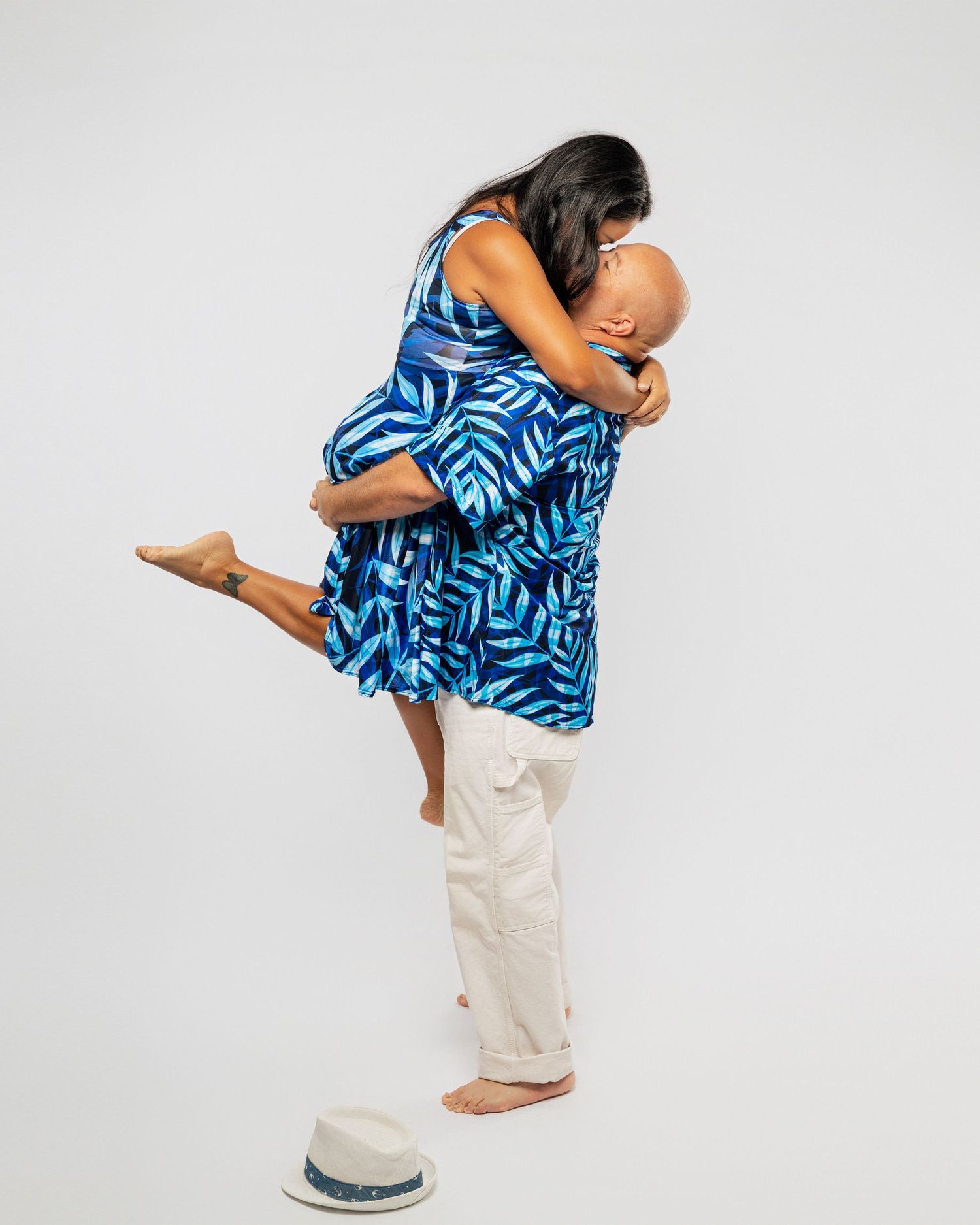 Couple embracing in casual blue print dress and white pants against white background.