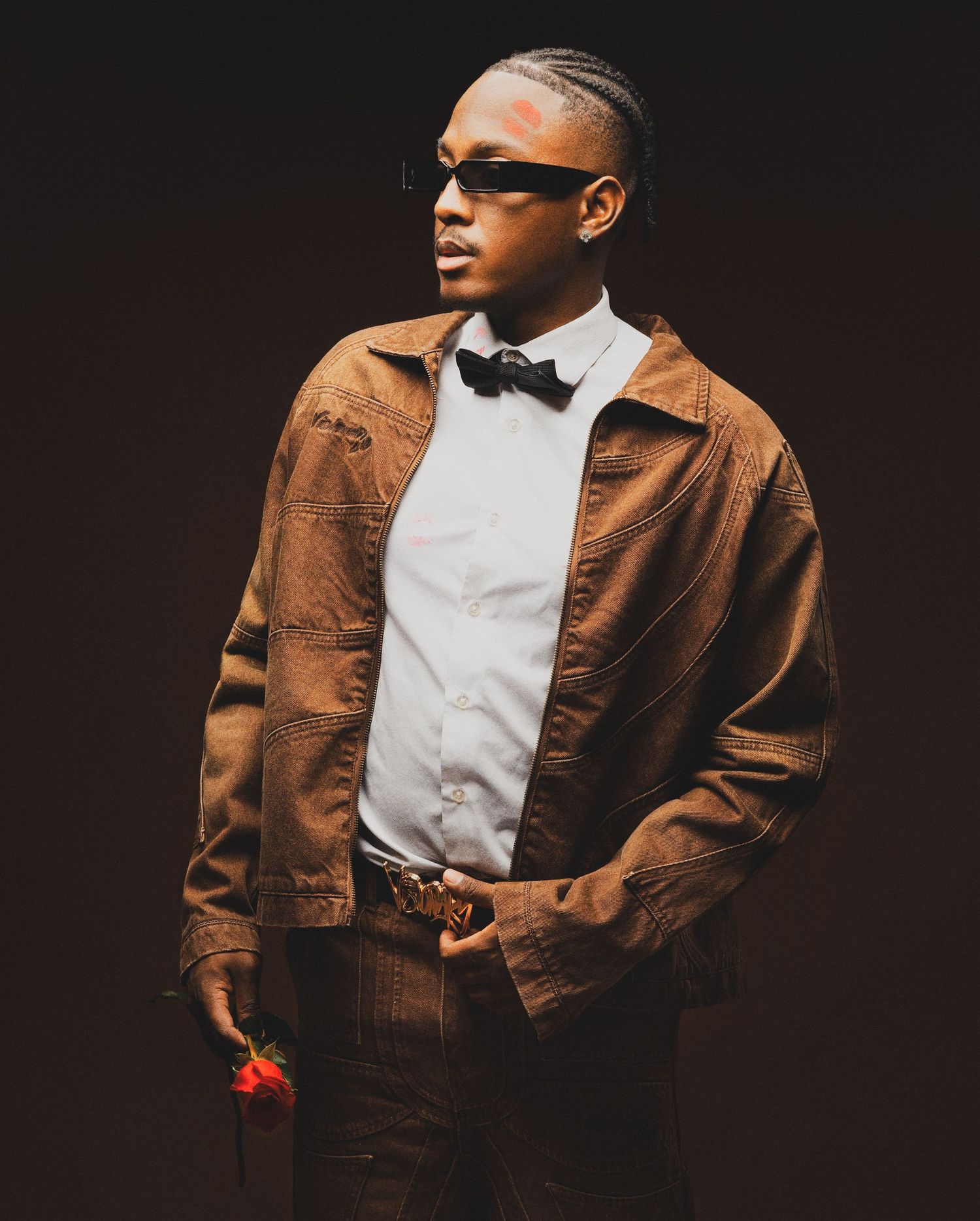 Stylish pose in formal attire with brown jacket and sunglasses holding red rose.