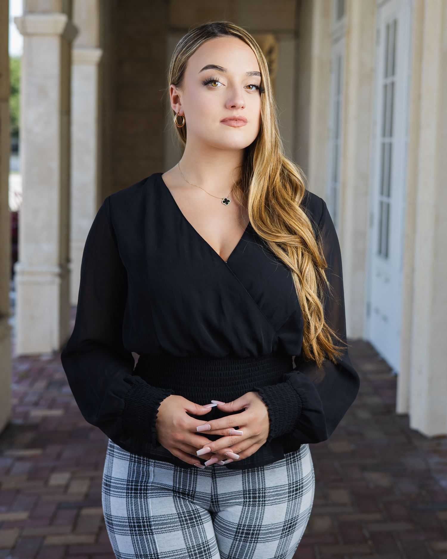 Professional portrait of a woman in a black wrap top and plaid pants standing in front of white columns.